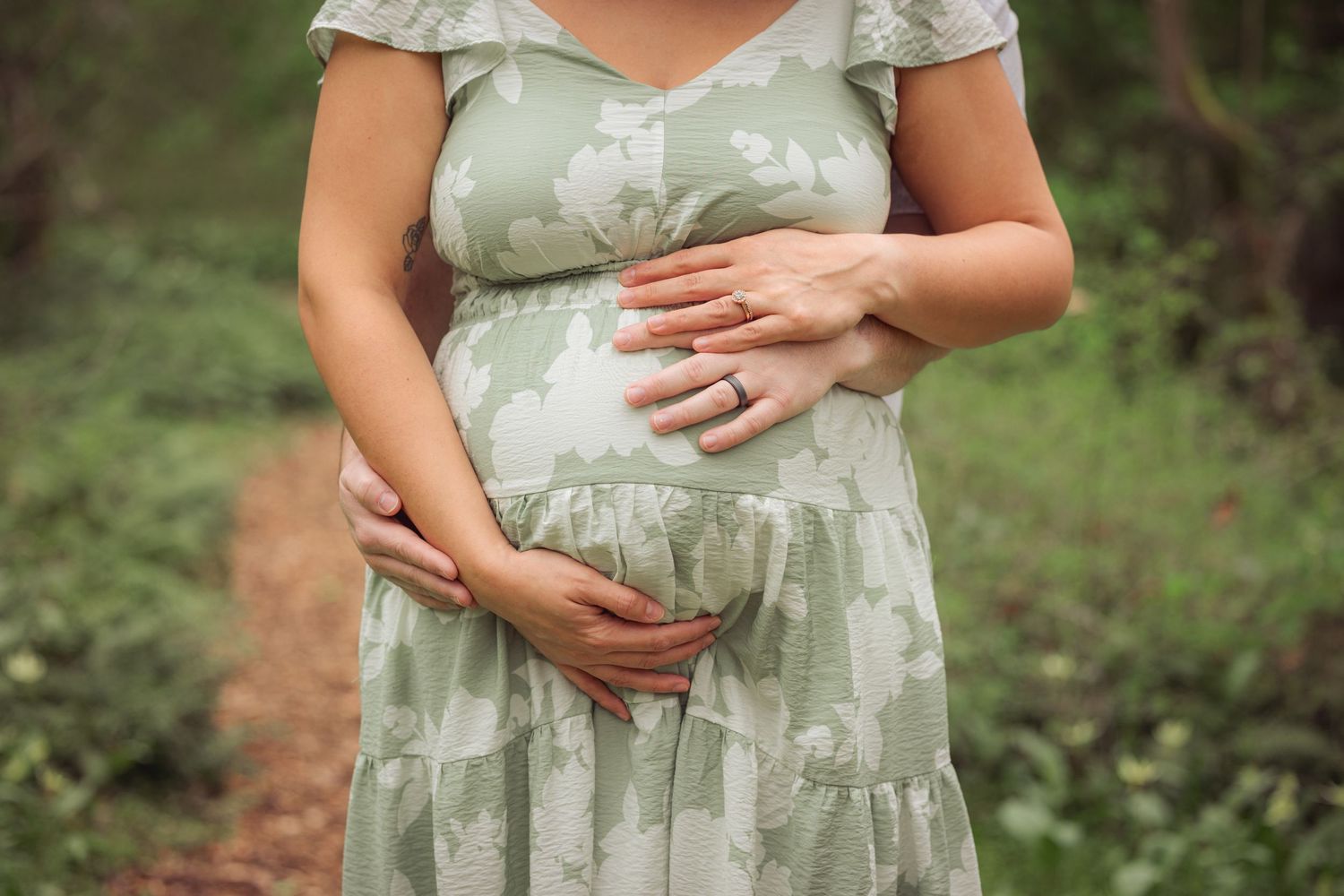 Woman in green floral dress cradling baby bump in outdoor maternity photo during a photo session by Salem, Oregon maternity photographer