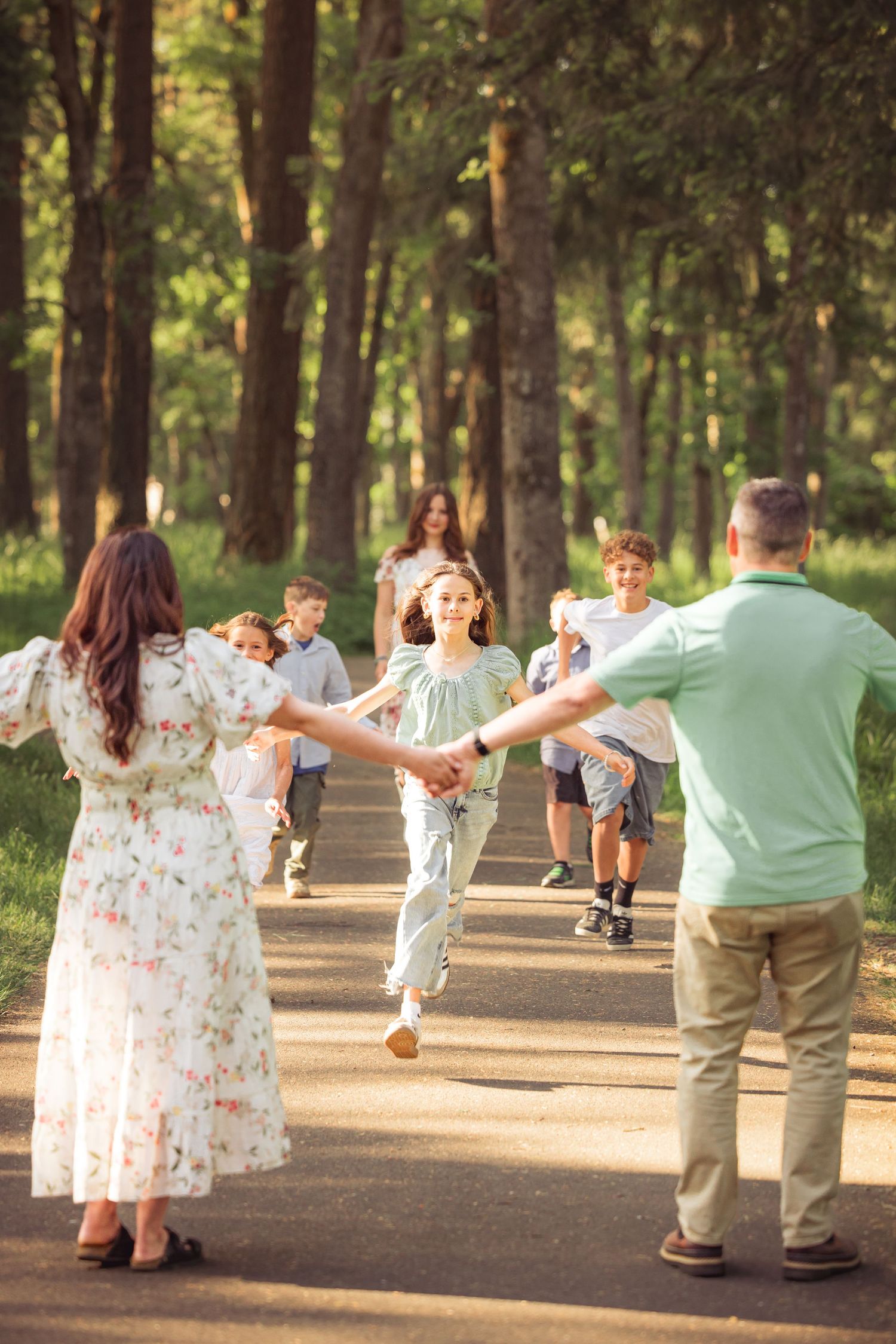 A group of people holding hands and dancing in a circle on a sunlit forest path, creating a joyful outdoor moment.