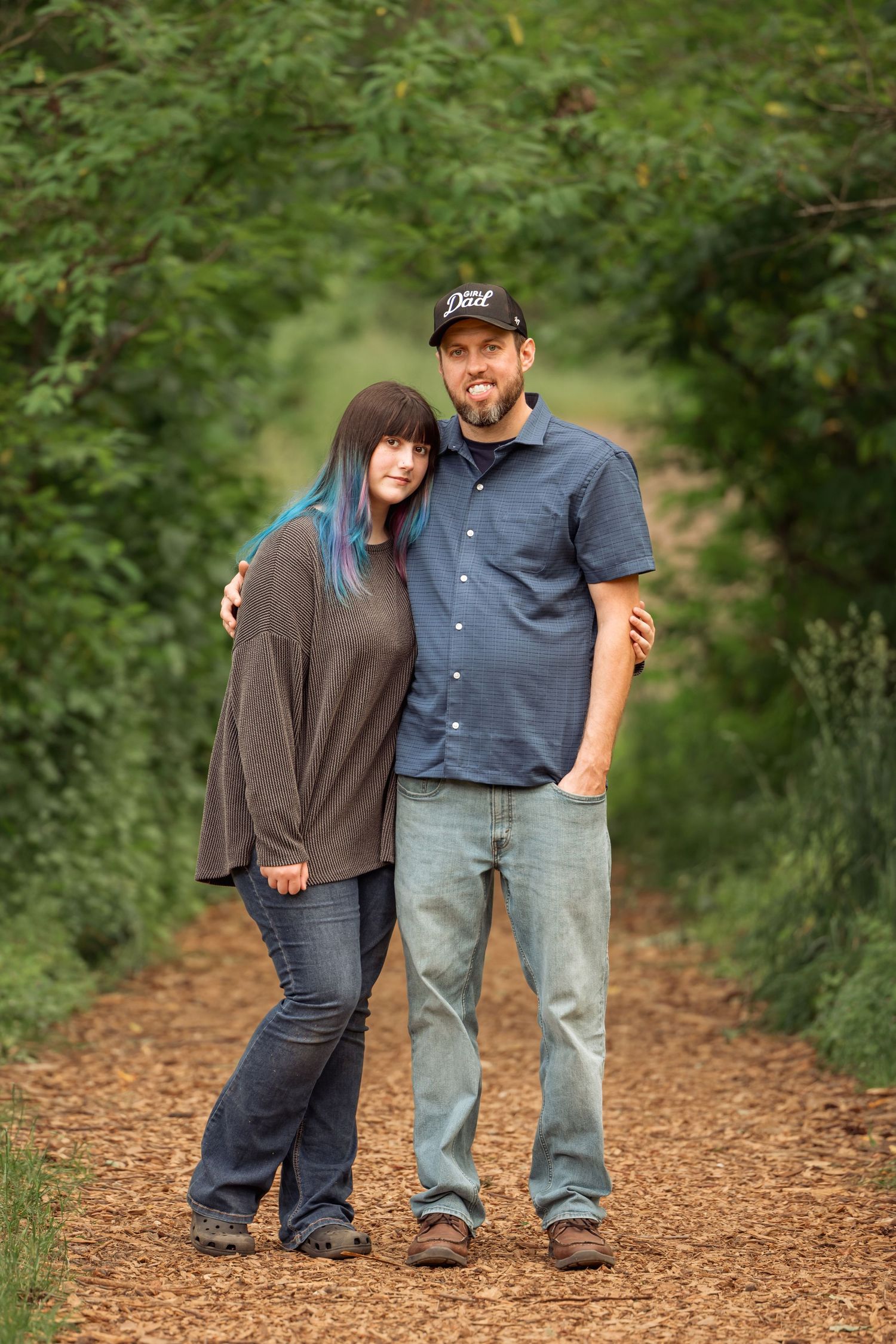 Two people stand together on a wood chip path surrounded by lush green foliage in a natural outdoor setting.