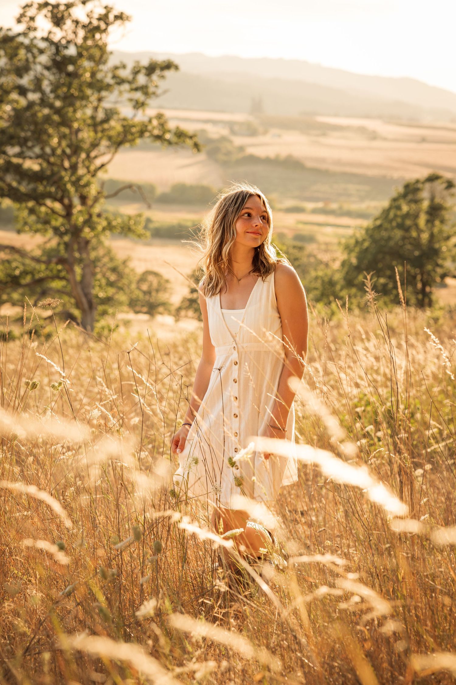 A dreamy golden hour portrait in a sun-drenched field of tall grass and wildflowers at sunset.