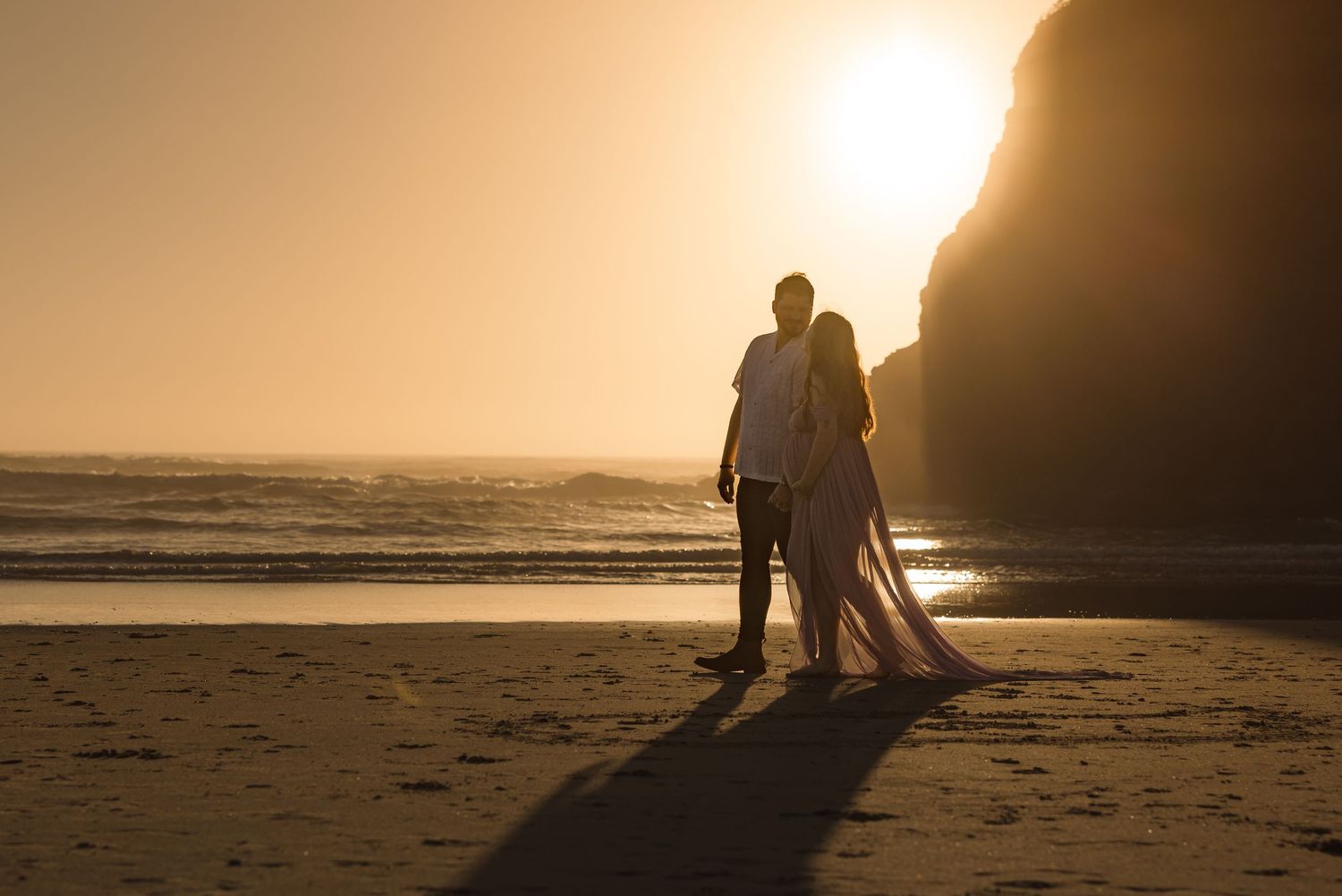 Silhouetted figures walk together on a beach at sunset with dramatic golden light streaming across the sand.