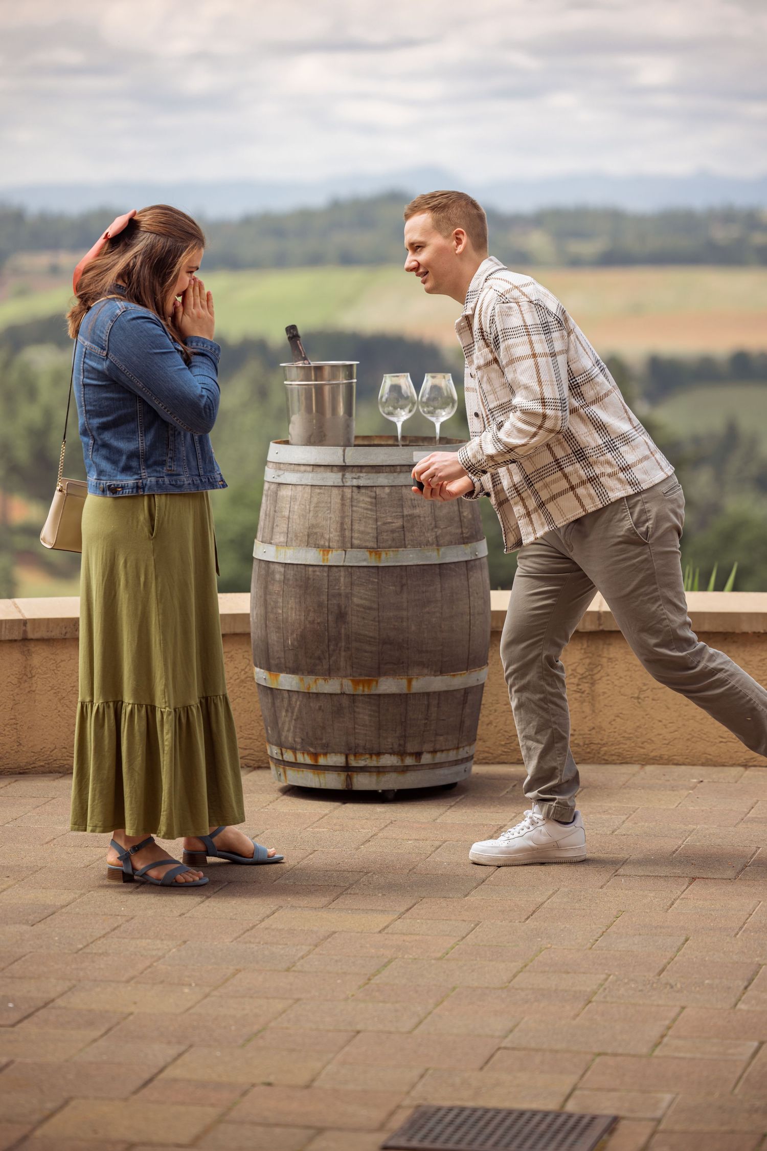 A surprise proposal scene on an outdoor terrace with a wine barrel and scenic mountain views.