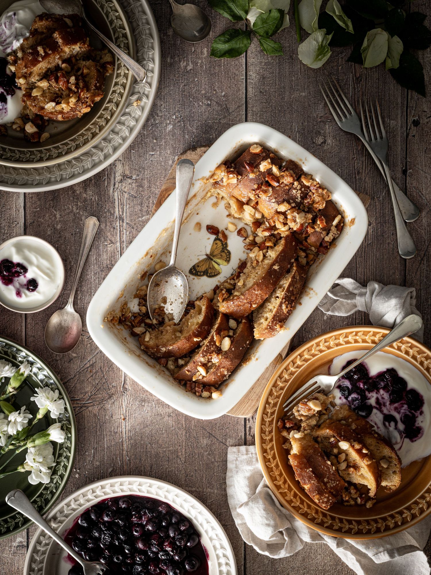 Flatlay view of a table laid with a baking dish and plates containing homemade baked French toast and smashed blueberries.