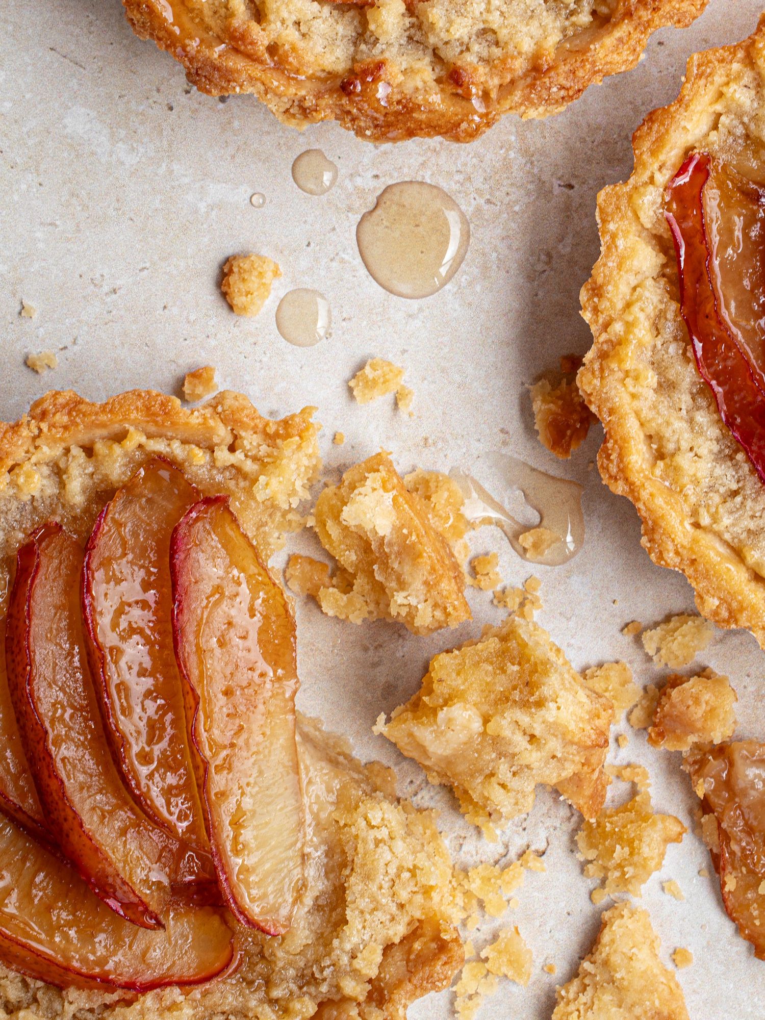 Close up of home baked plum frangipane tarts on a table, showing crumbly pastry and honey glazed plums.