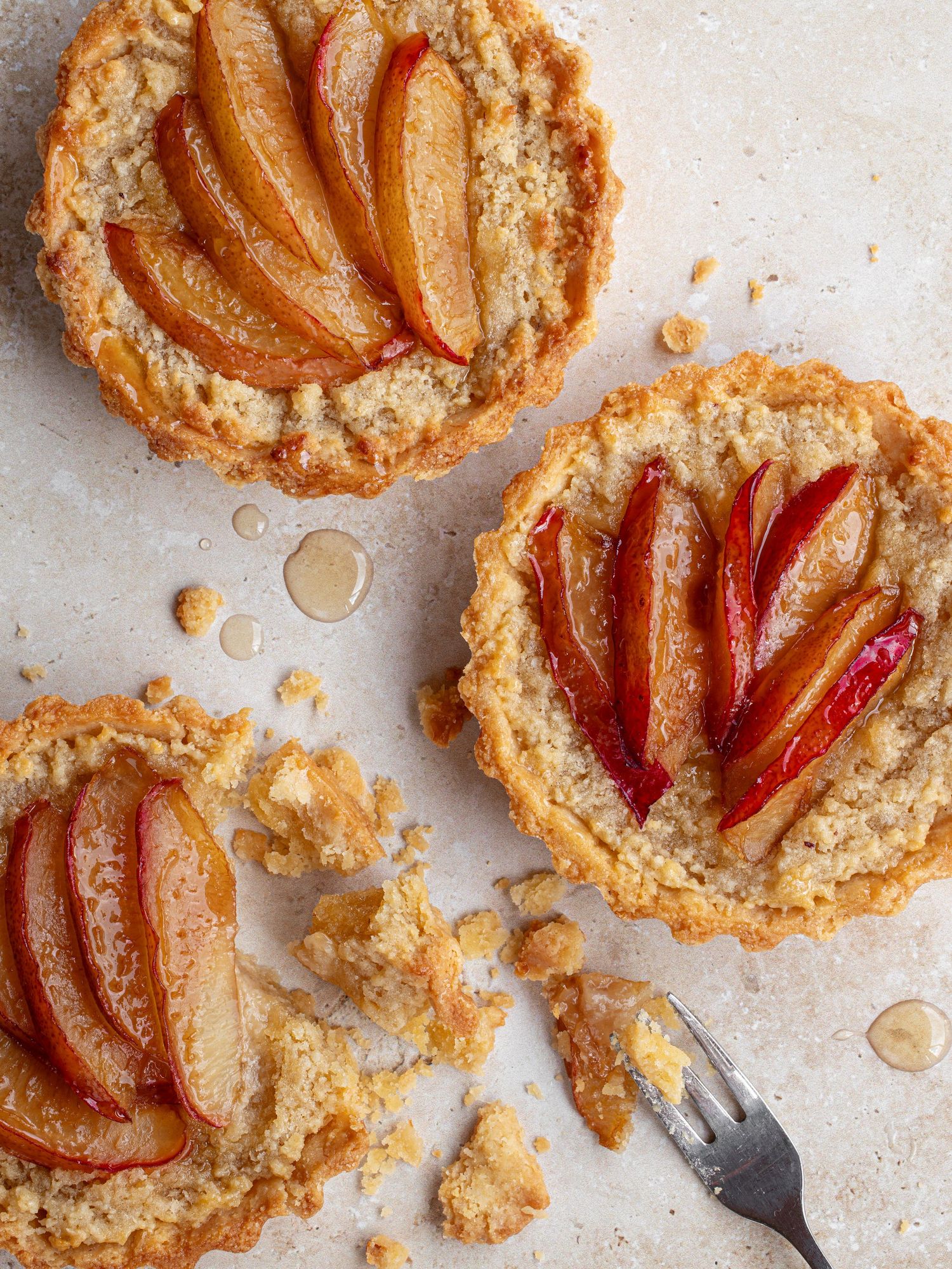 Home baked plum frangipane tarts on a table, showing crumbly pastry and honey glazed plums.