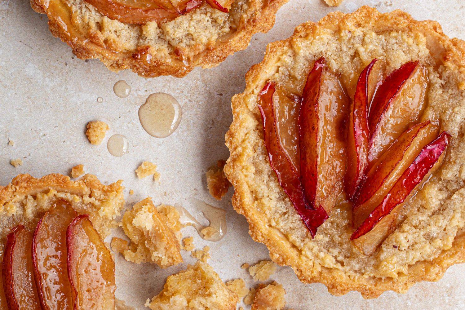 Home baked plum frangipane tarts on a table, showing crumbly pastry and honey glazed plums.