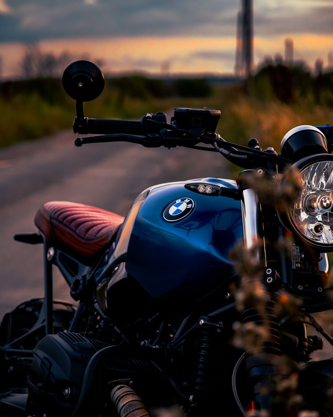 BMW motorcycle with blue tank and brown leather seat parked on road during dramatic sunset.