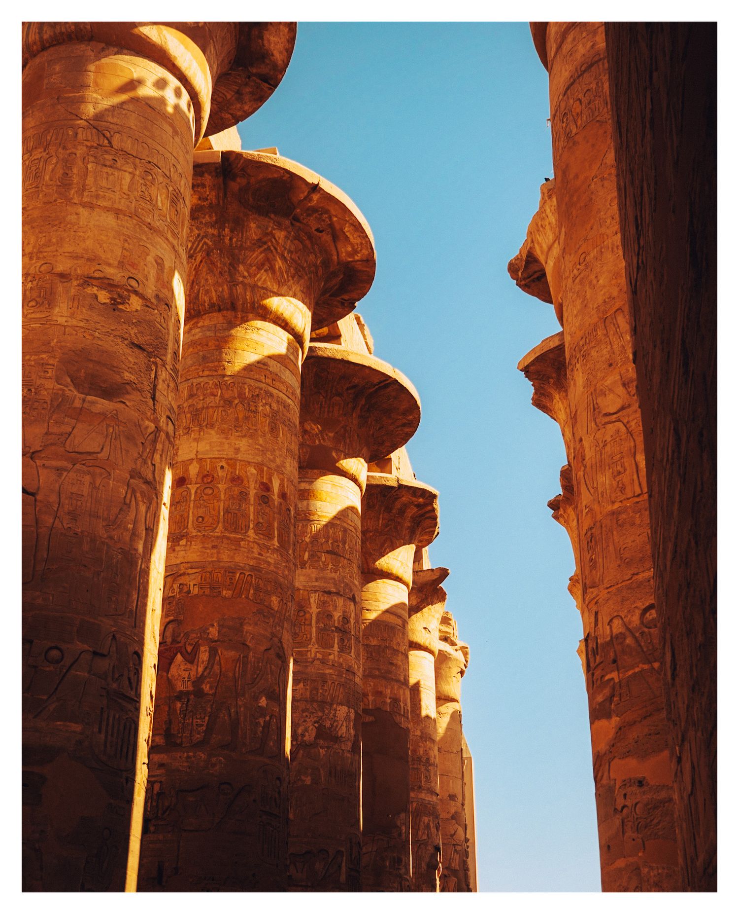 Massive stone columns at the Great Hypostyle Hall in Karnak Temple cast dramatic shadows under blue Egyptian skies.