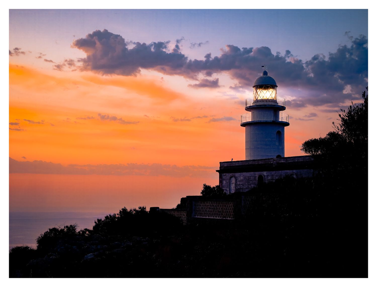 A dramatic panoramic view of a lighthouse silhouetted against a vibrant orange and purple sunset sky.