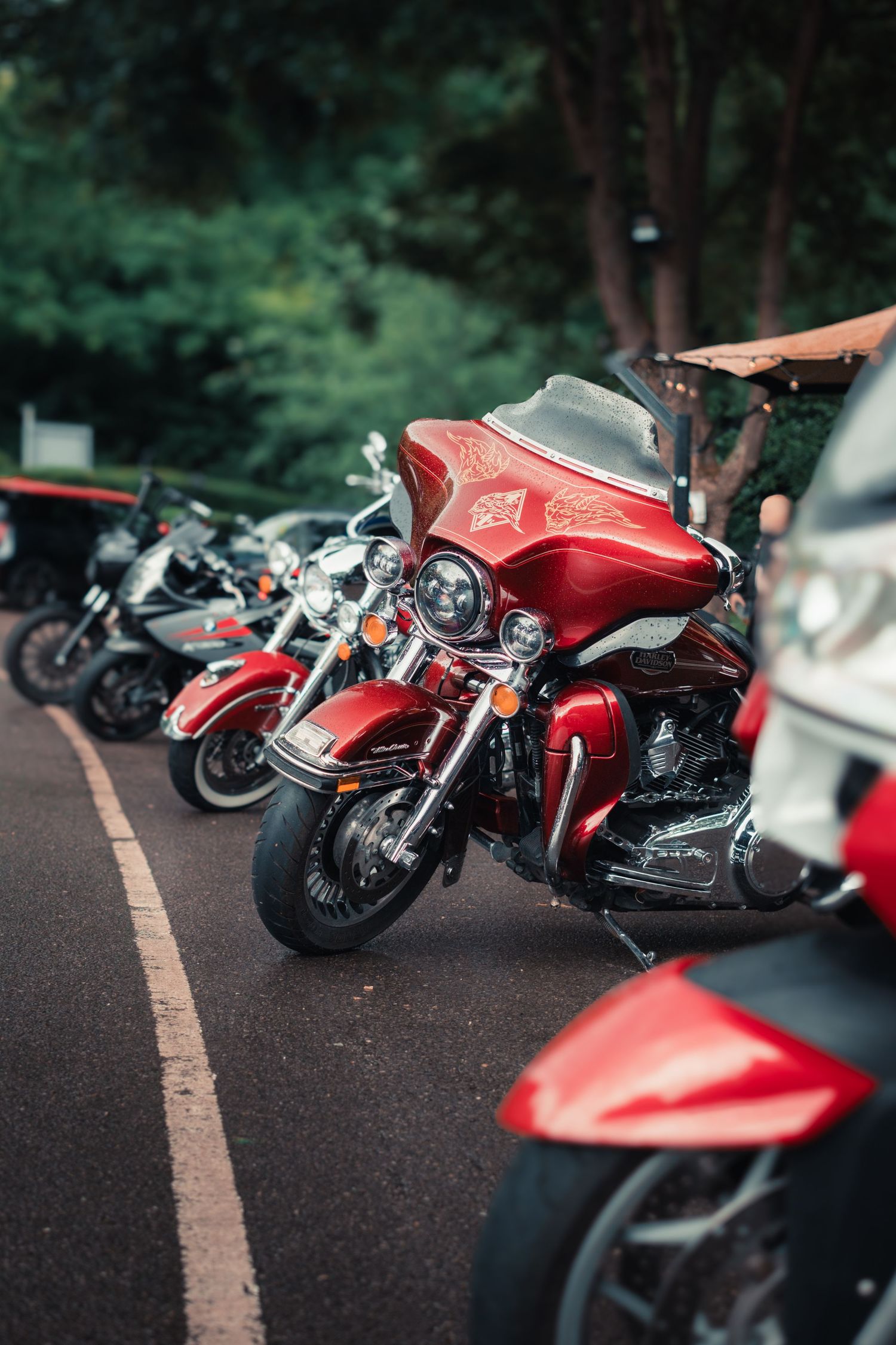 A row of red custom motorcycles parked in a shaded outdoor lot showing different angles of their sleek designs.