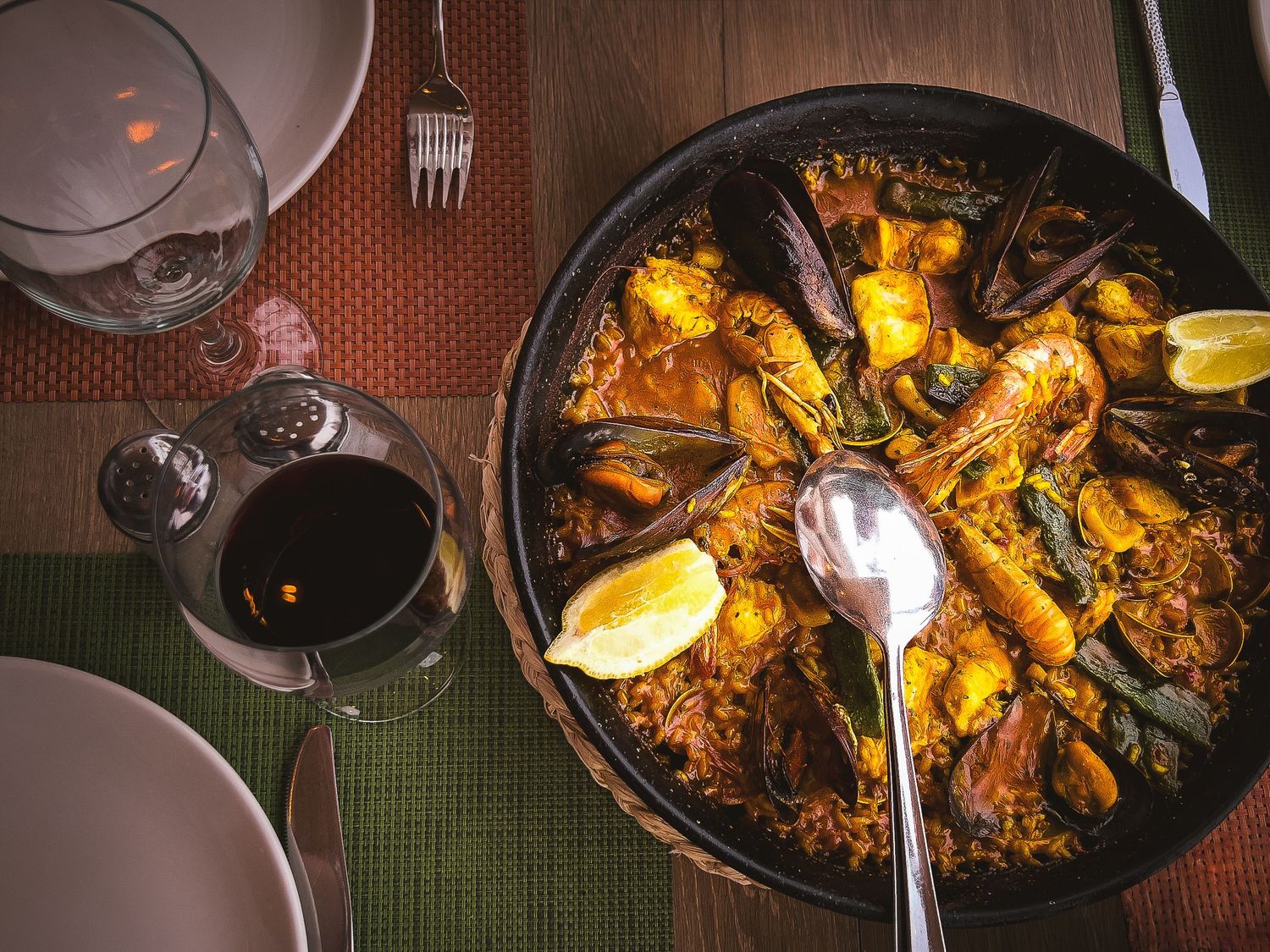 Traditional Spanish seafood paella with mussels, shrimp and lemon wedges served in black pan with red wine.