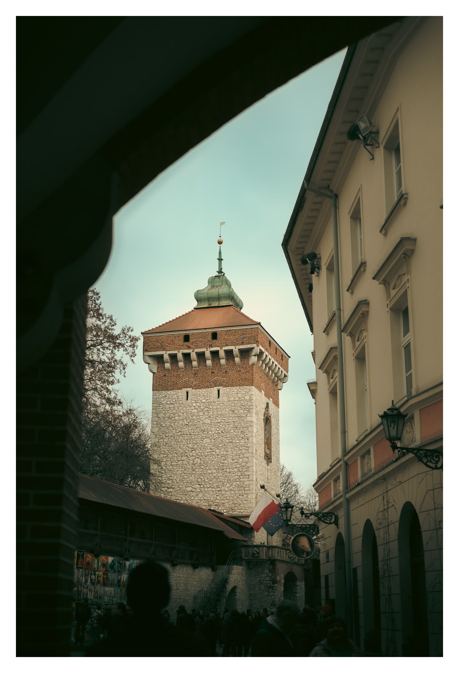 Medieval stone tower of St. Florian's Gate viewed through an archway in Krakow's historic Old Town district.