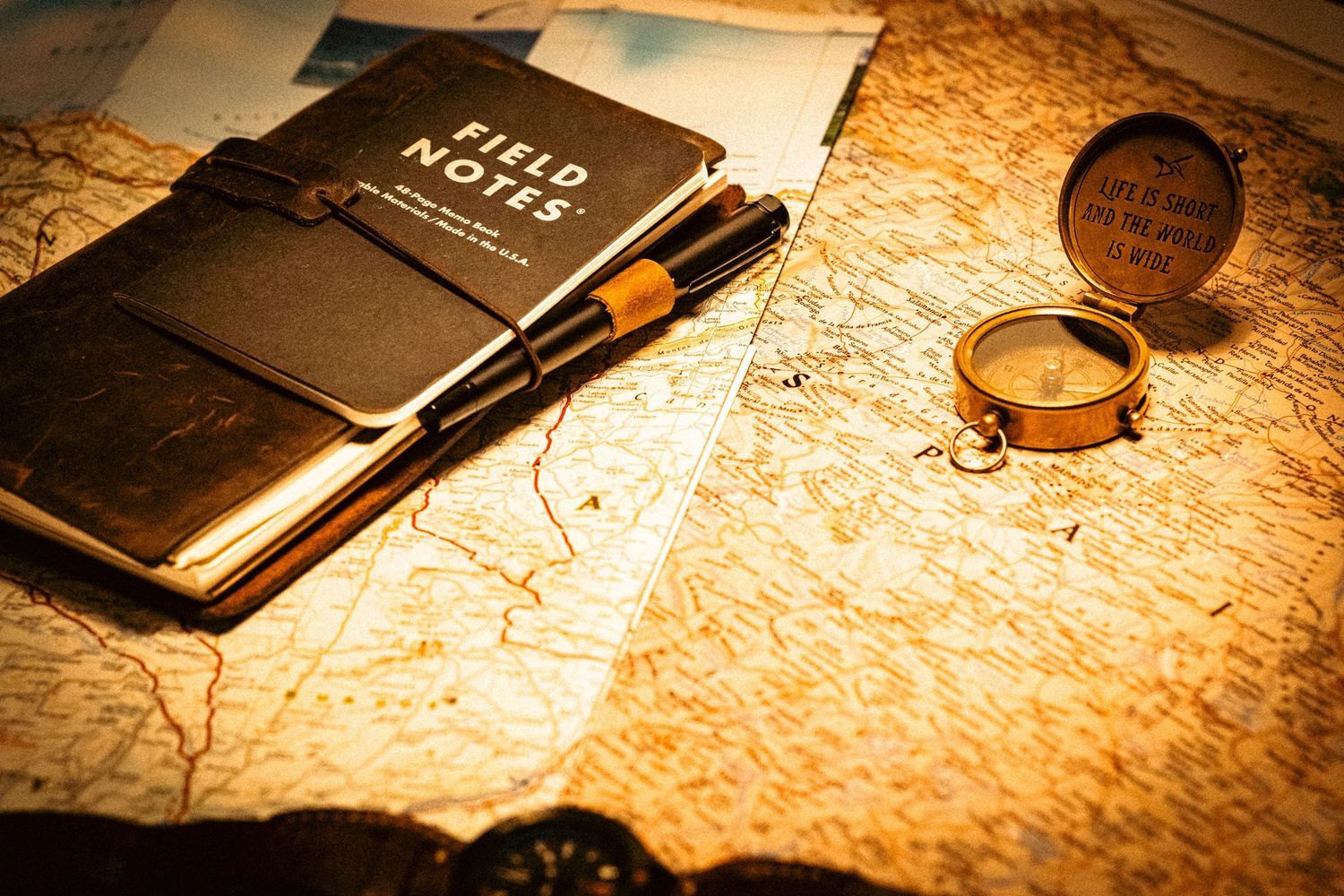 A vintage travel journal and fountain pen lay beside a brass compass on an aged sepia map.