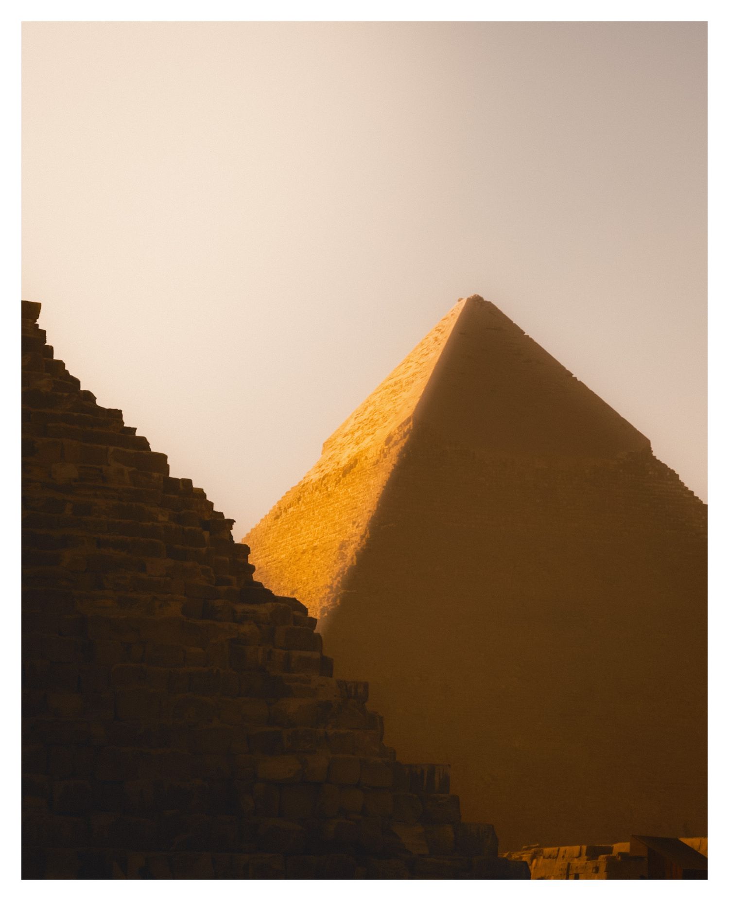 Ancient Egyptian pyramids cast dramatic shadows at sunset with golden sunlight illuminating one pyramid's face.