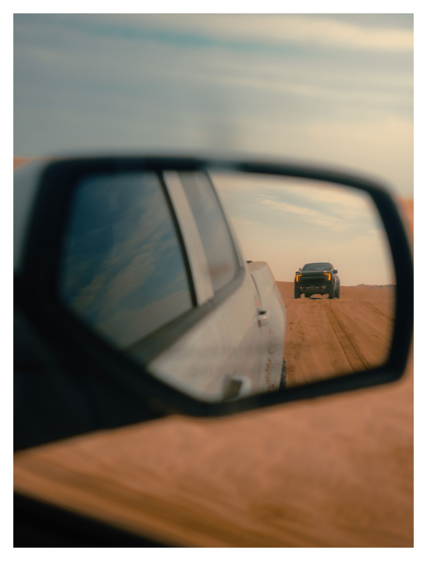 A series of car side mirror views showing a vehicle following on a dusty dirt road during sunset.