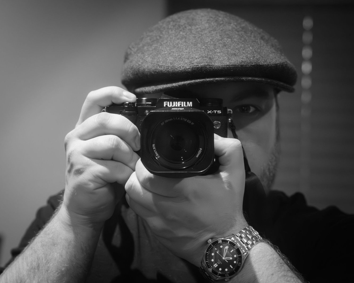 A hand holds a Fujifilm camera against a dark background, showing a series of similar camera-holding poses in black and white.