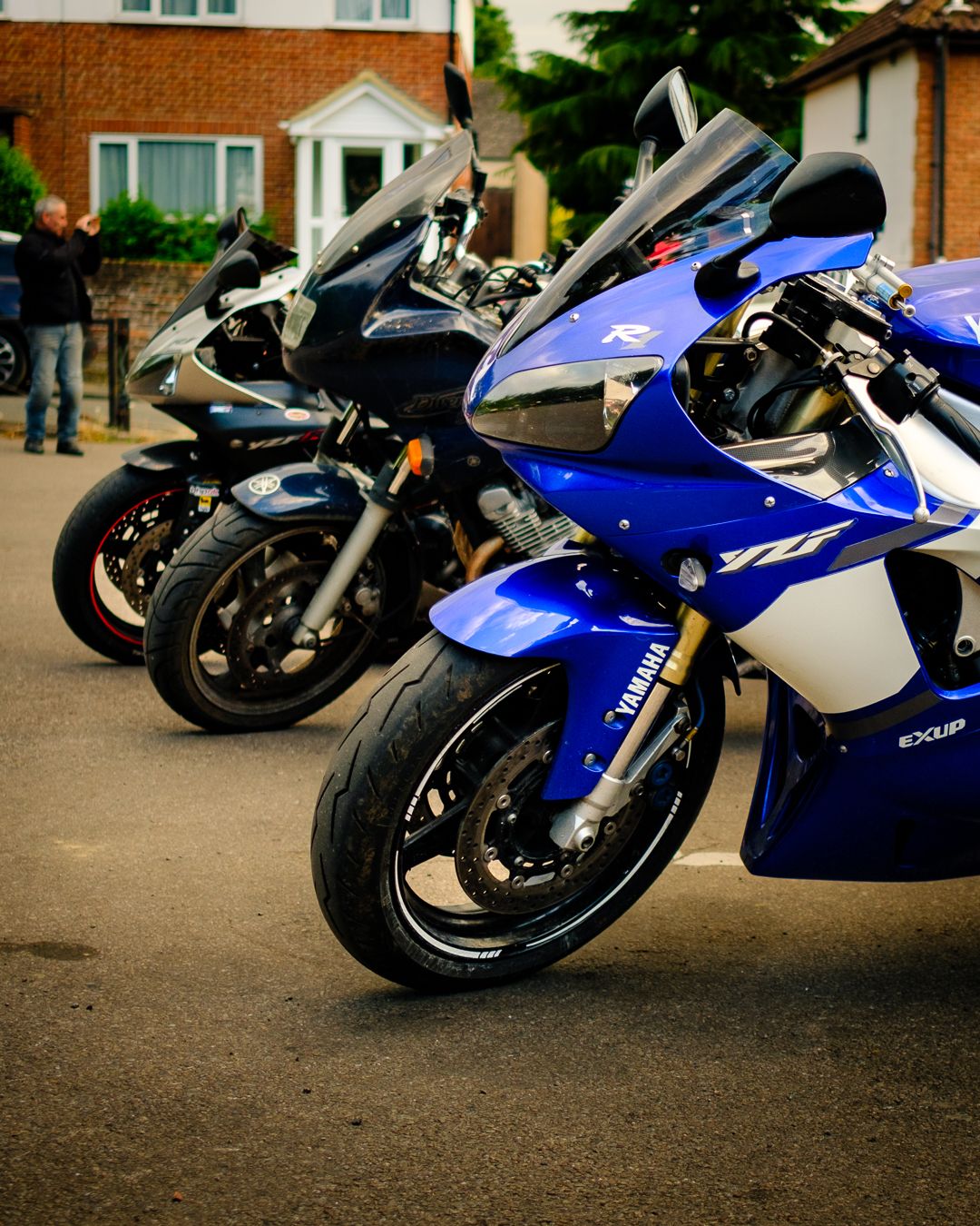 Two sporty motorcycles parked side by side, one blue and white Yamaha R6 and one black bike on a residential driveway.