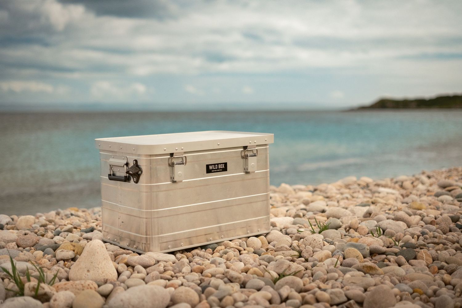 Metal storage container sits on rocky beach shoreline against cloudy coastal backdrop.