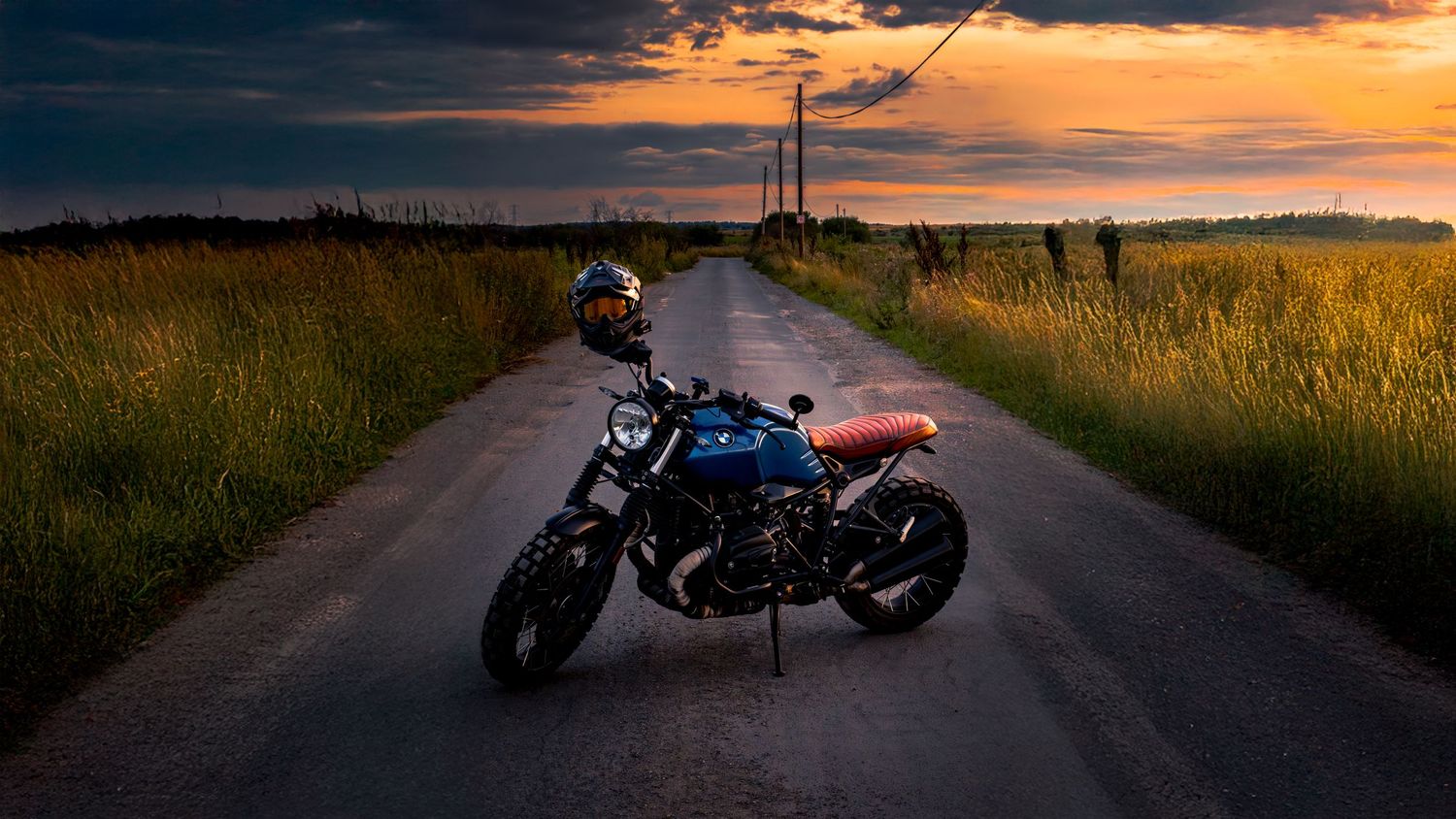 Dramatic panoramic sunset over a rural road with silhouetted power lines against an orange sky.