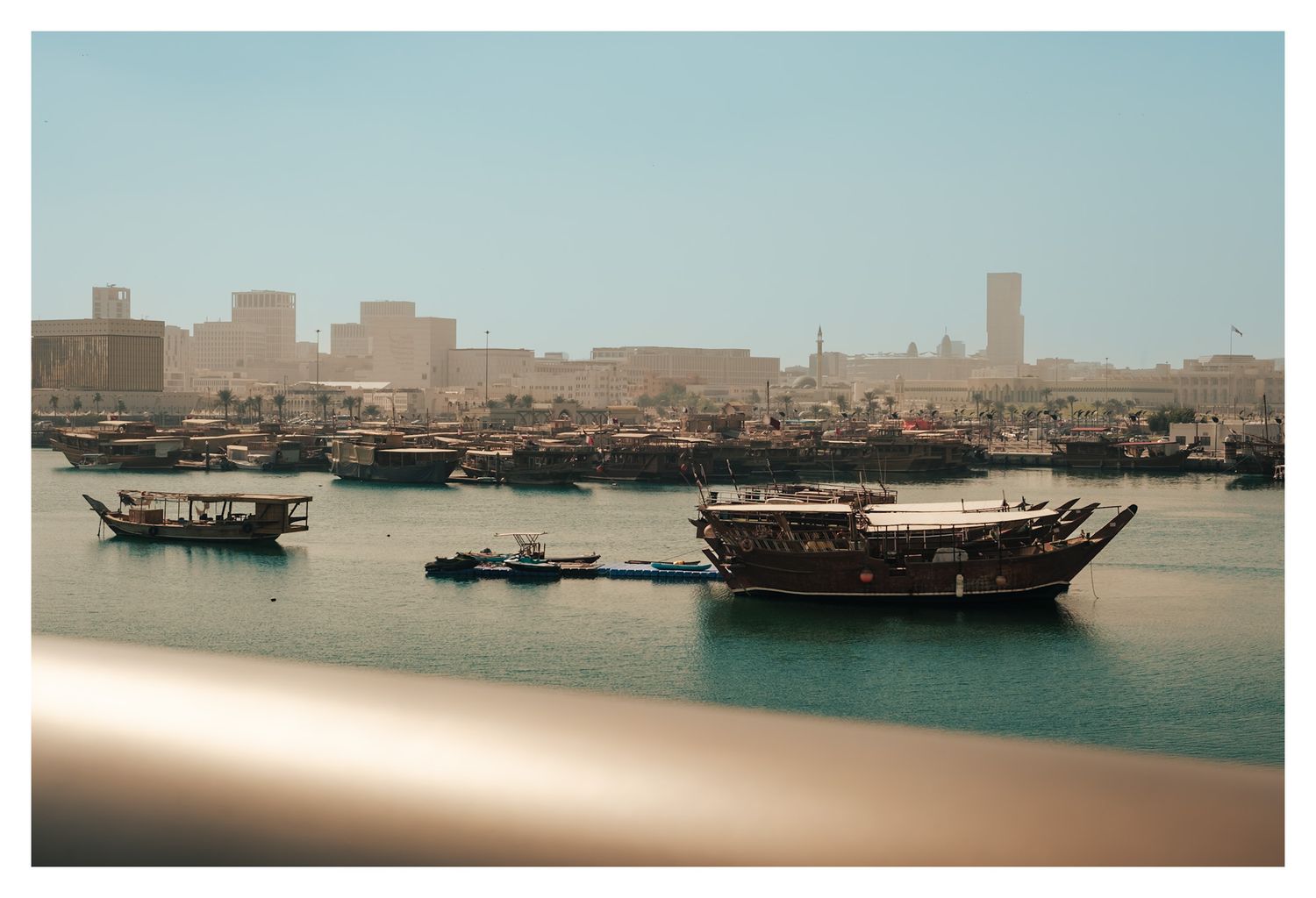 Panoramic view of traditional wooden dhow boats in the harbor with city skyline in the background.