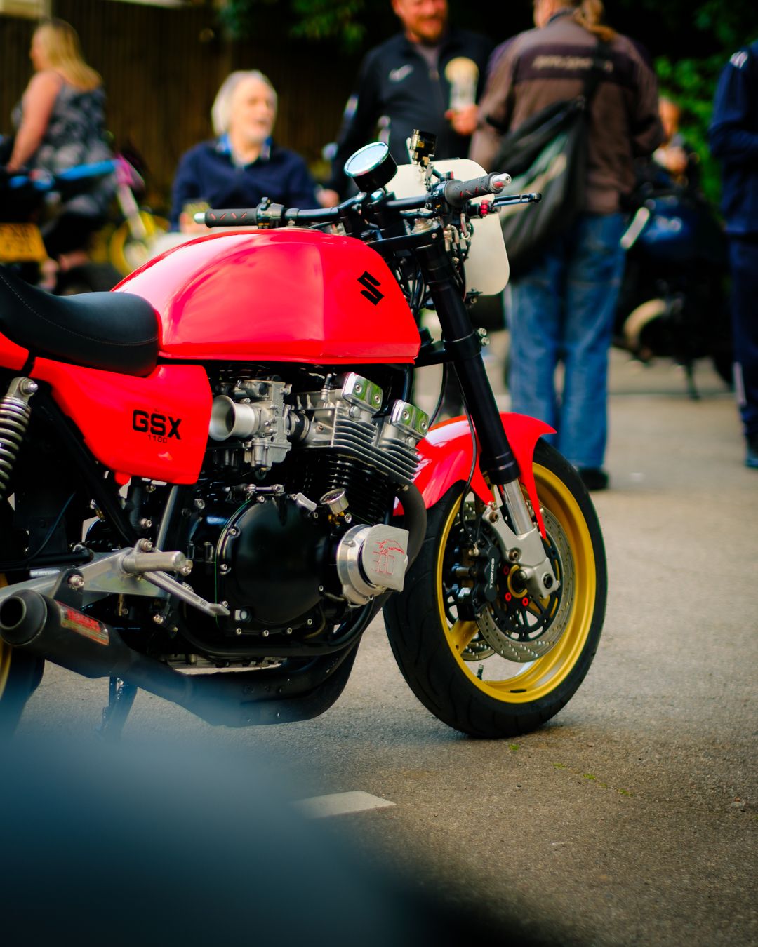 Classic red Honda CB cafe racer motorcycle with gold wheels parked at an outdoor event.