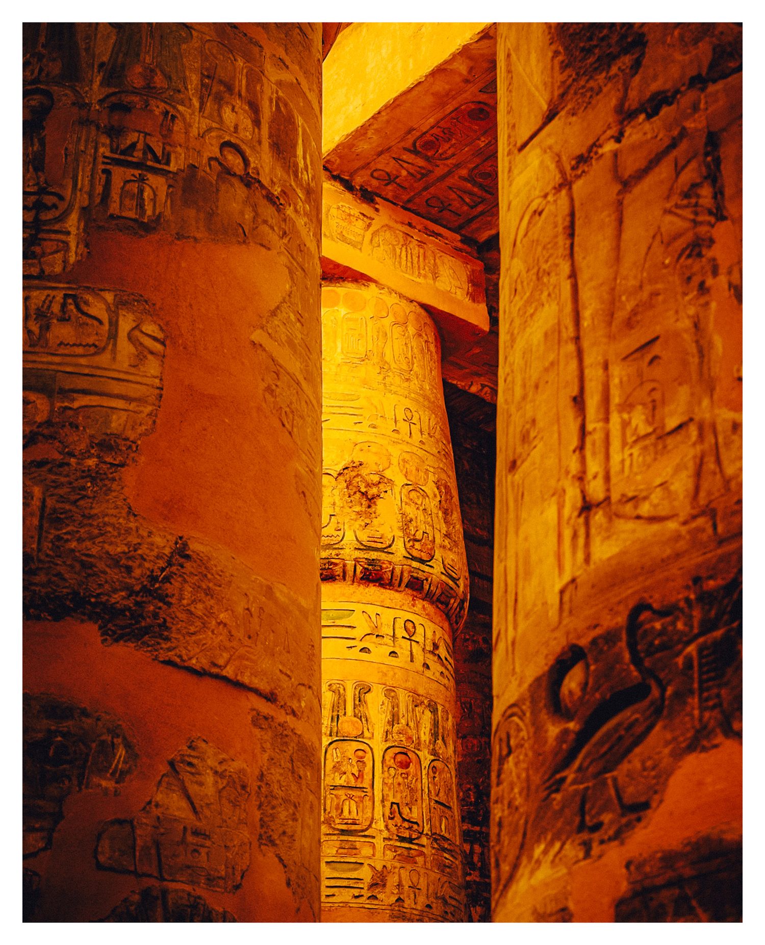 Ancient Egyptian hieroglyphic columns illuminated in warm golden light at Karnak Temple showcase detailed carved inscriptions.