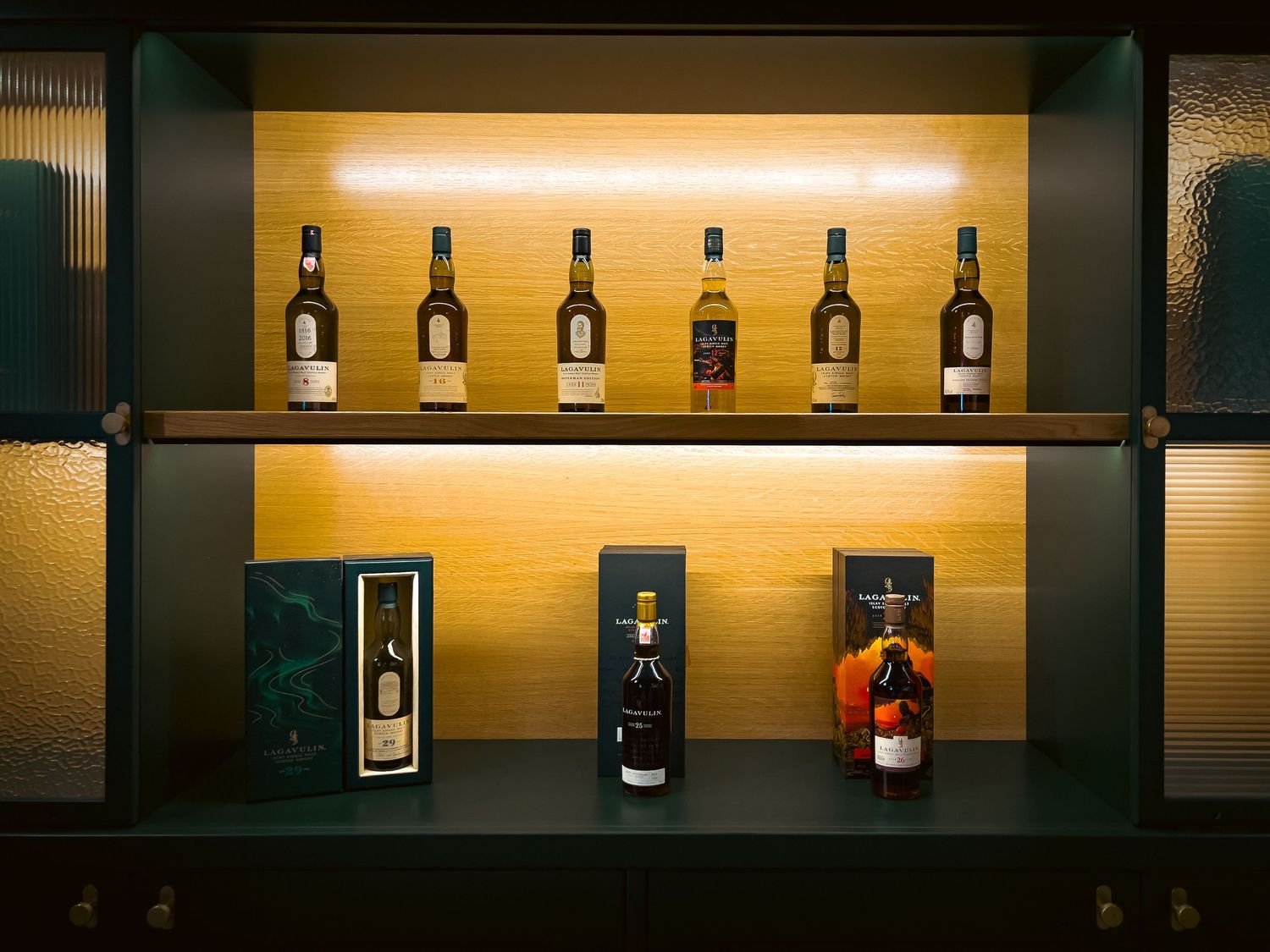Row of illuminated whisky bottles on dark wood shelves with warm lighting creates an elegant bar display ambiance.
