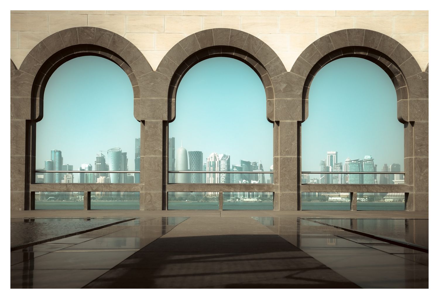 Architectural series of arched windows overlooking a city skyline with turquoise sky in the background.