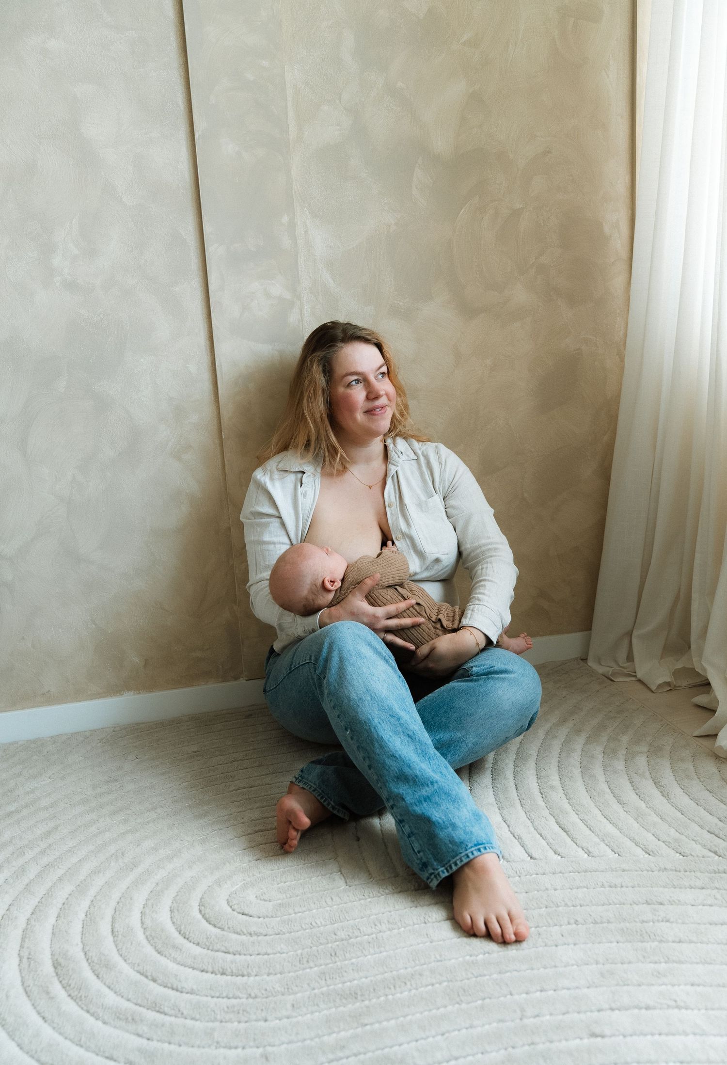 Moeder kijkt blij uit het raam naar de lucht terwijl haar baby aan de borst ligt – Myrthegwen Fotografie Groningen