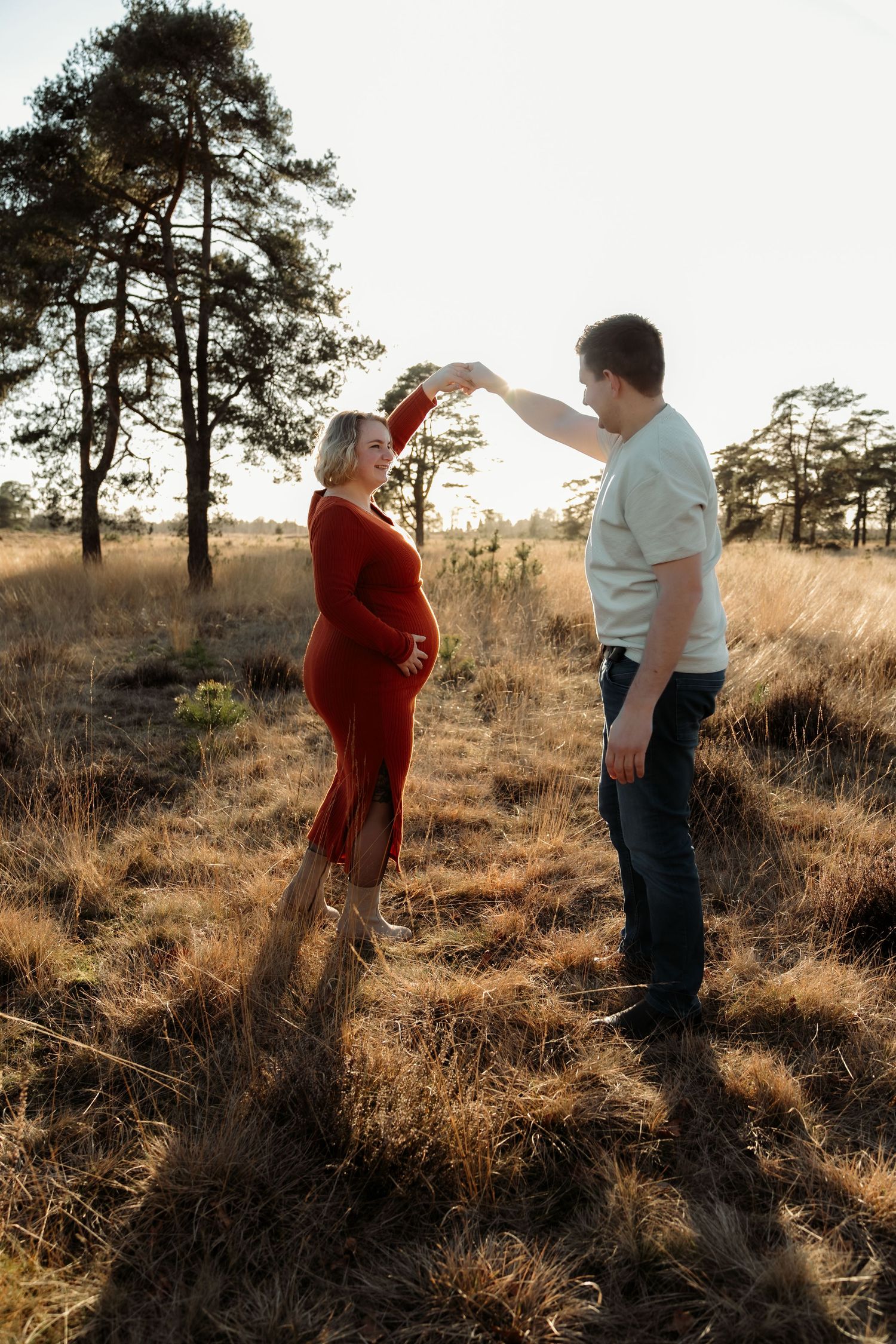 Blije zwangere vrouw en man staan samen in de natuur bij zonsondergang – Myrthegwen Fotografie Groningen