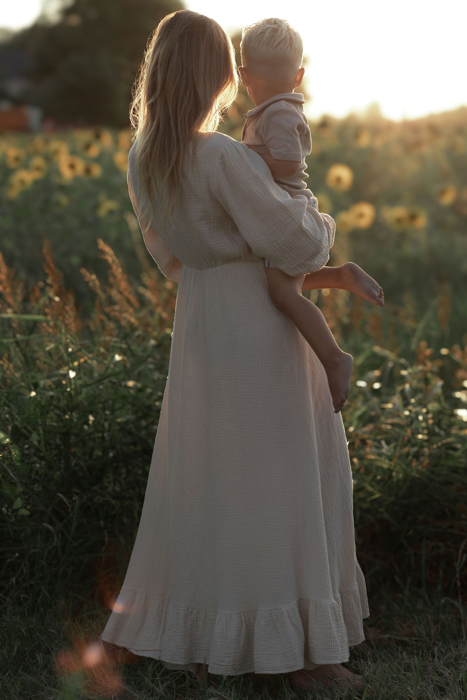 Moeder en zoontje poseren in een veld met zonnebloemen bij zonsondergang, vastgelegd door Myrthegwen Fotografie Groningen.