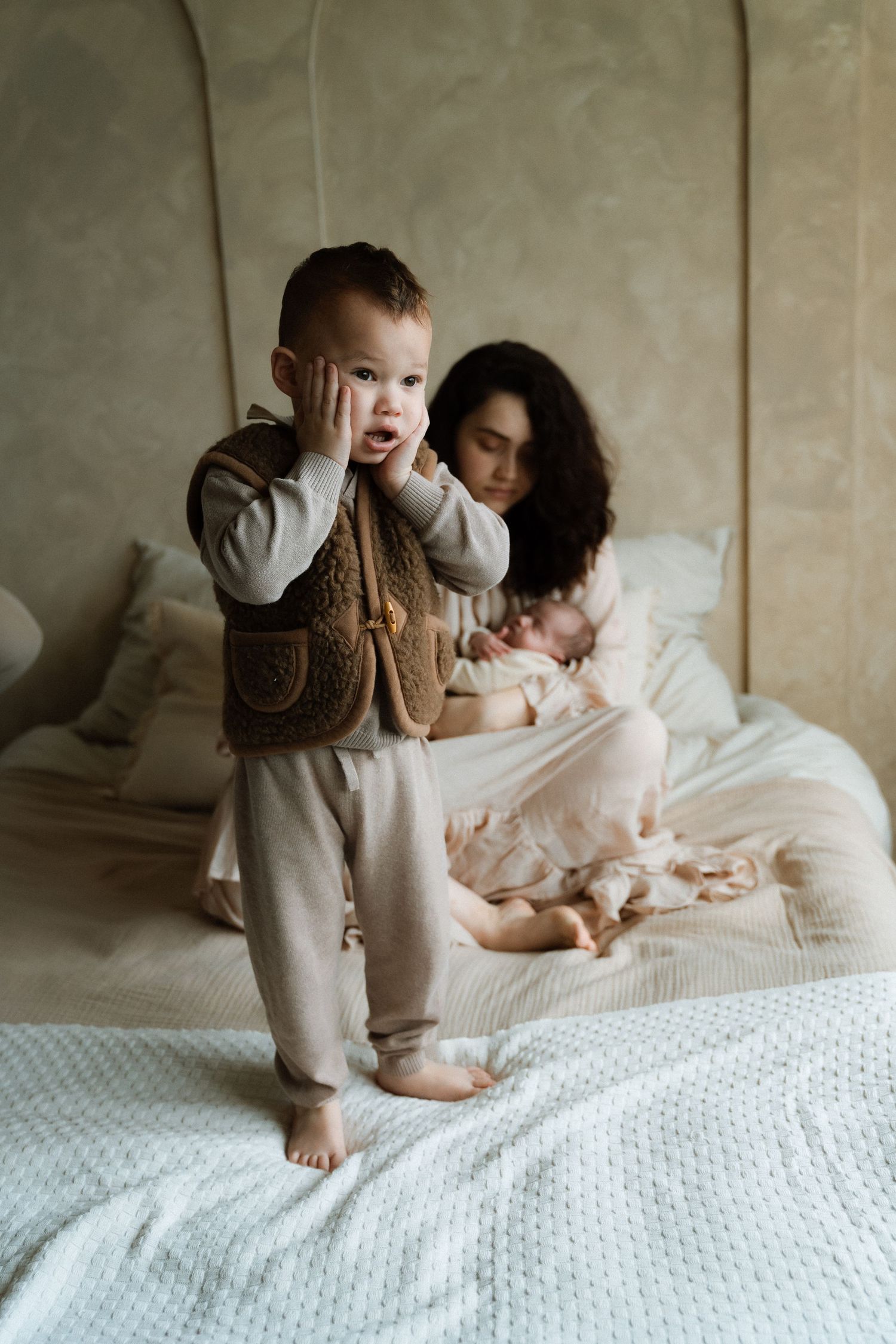 Moeder met pasgeboren baby op de achtergrond, kleuter staat op de voorgrond met een geschrokken blik – Myrthegwen Fotografie Groningen