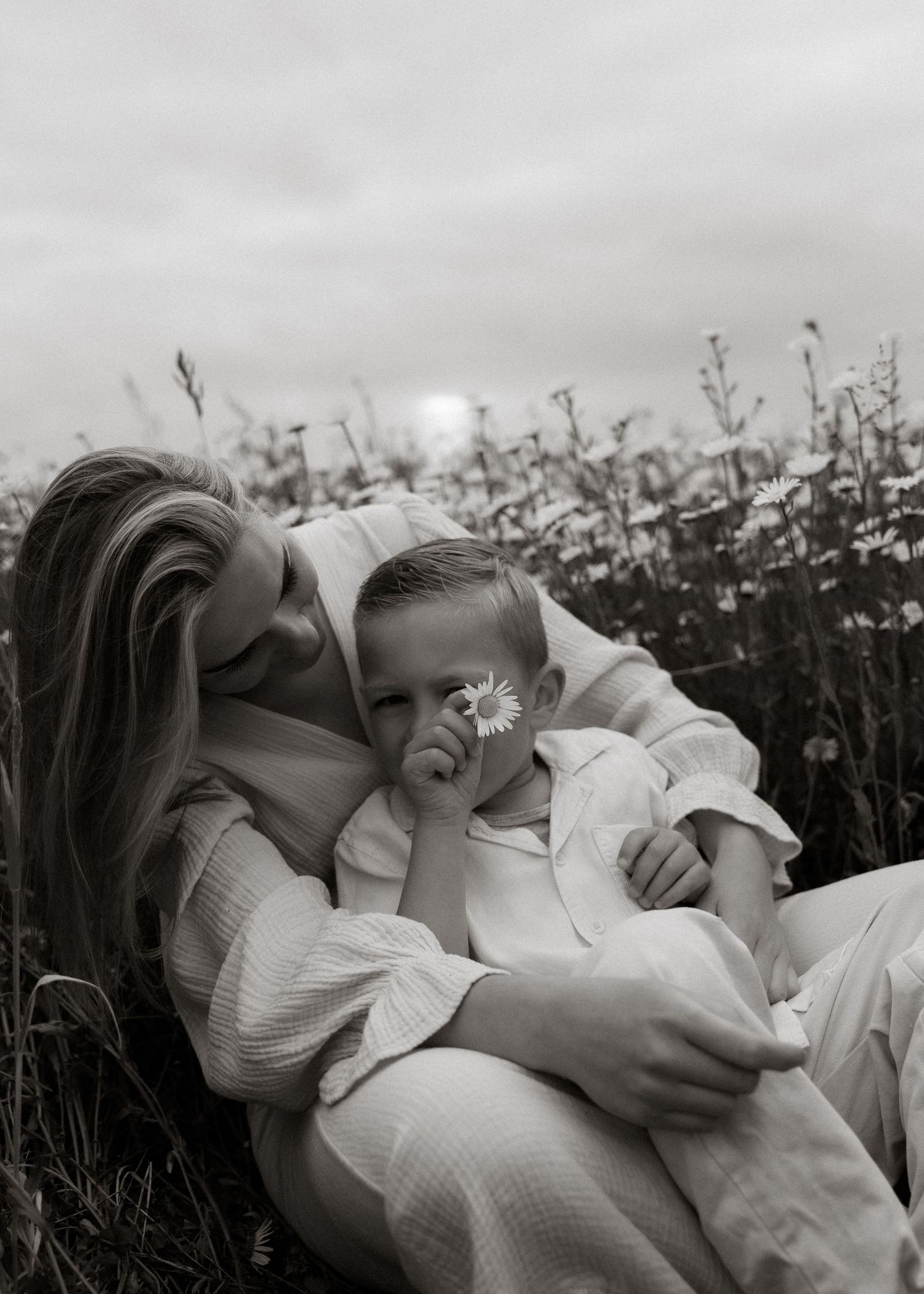 Prachtig zwart-wit portret van een moeder en kind met bloem in een veld, vastgelegd door Myrthegwenfotografie.