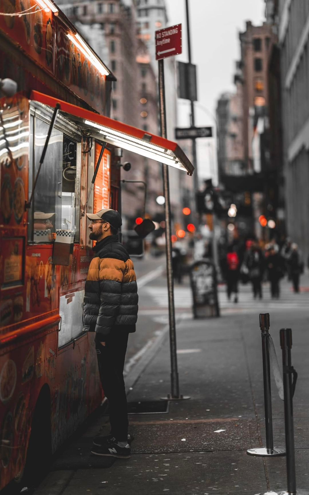 People waiting at food truck with red lighting in black and white urban setting.