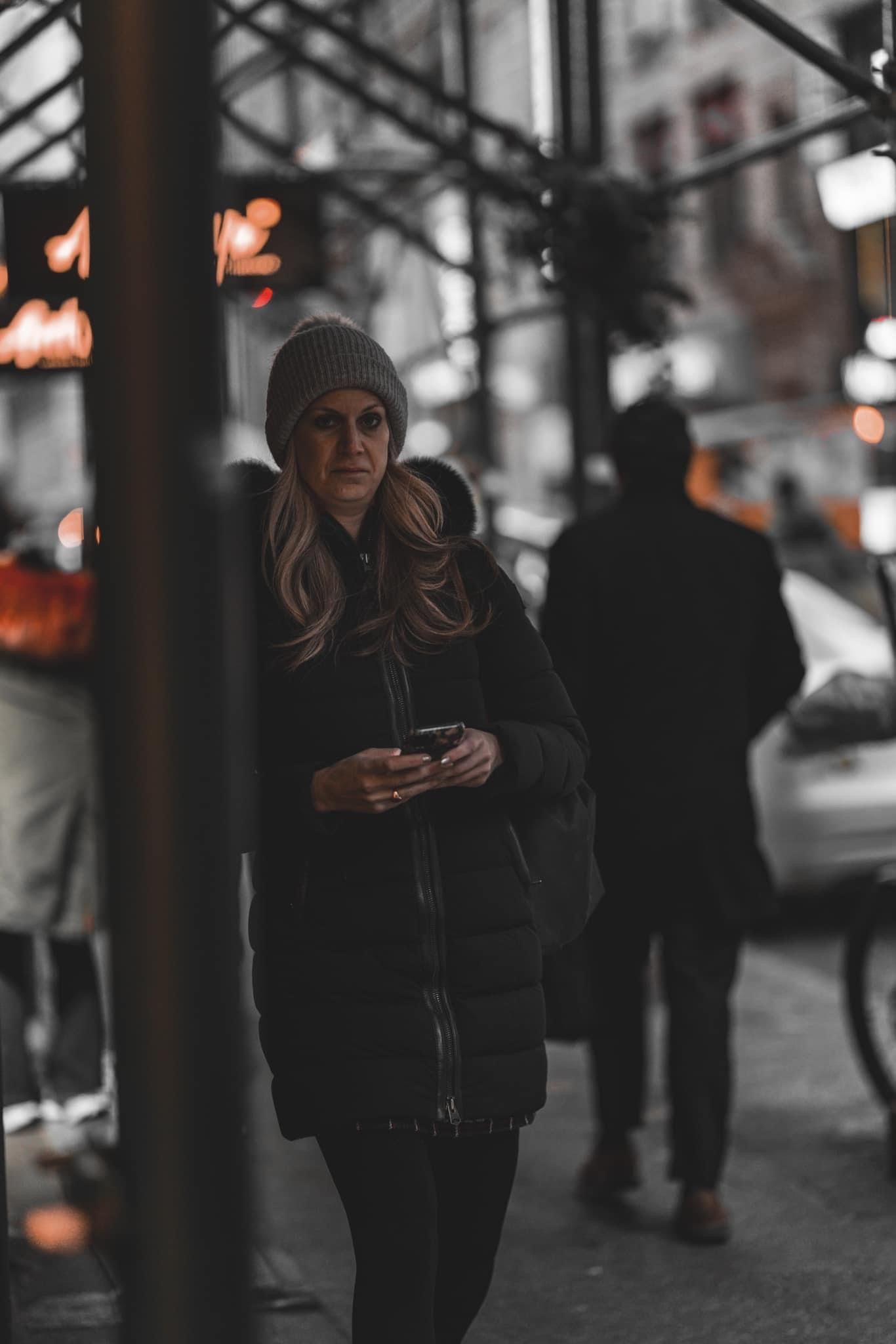People in dark winter clothing walking along a dimly lit urban sidewalk.