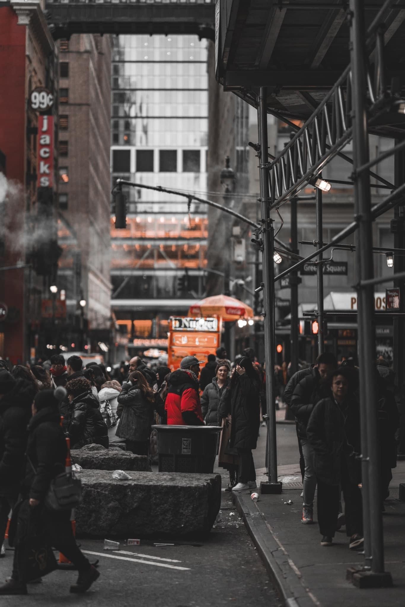 Urban street scene with people waiting in a covered area with orange accents and black and white tones.