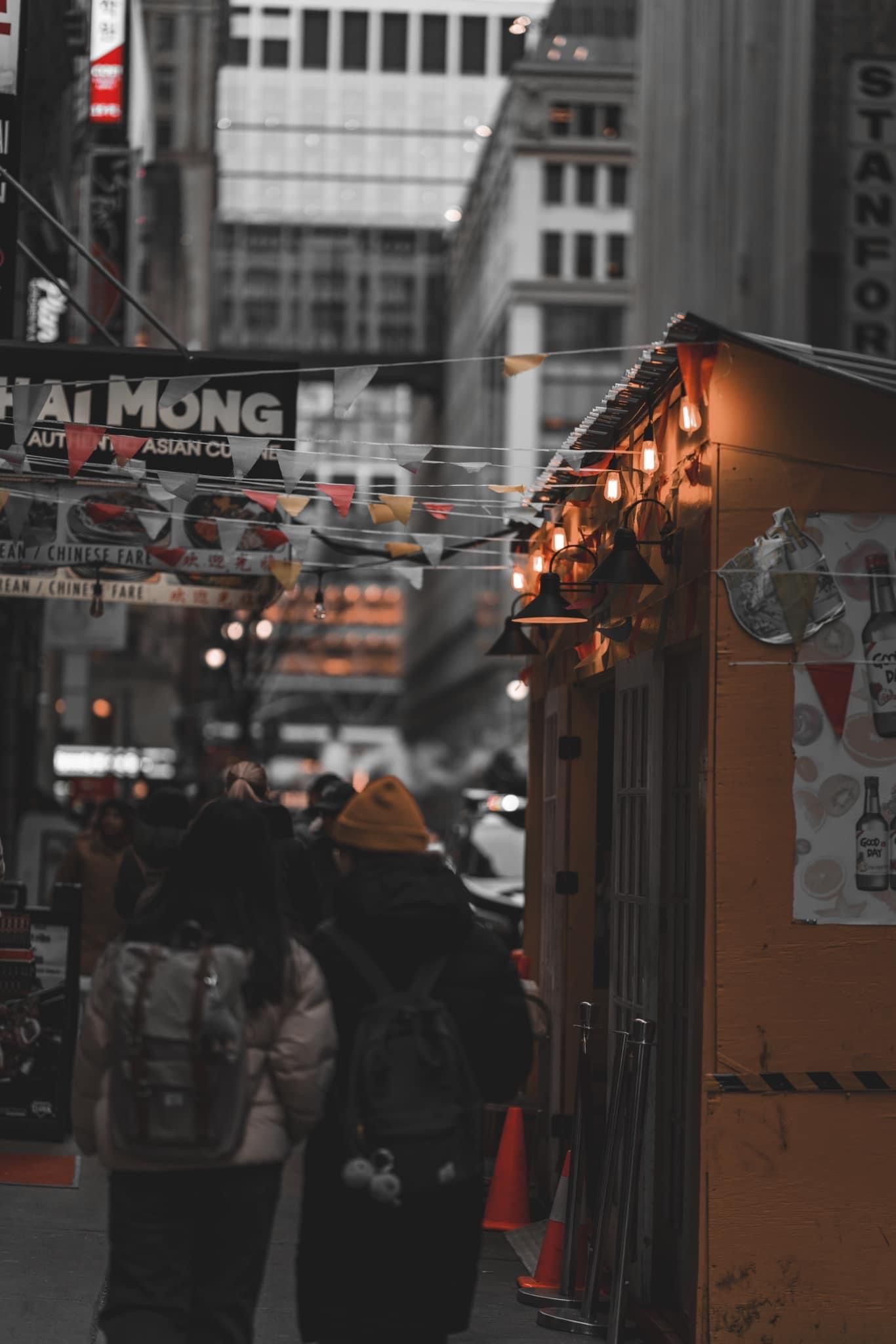 Night street scene with orange-lit food stalls and pedestrians in an urban setting.