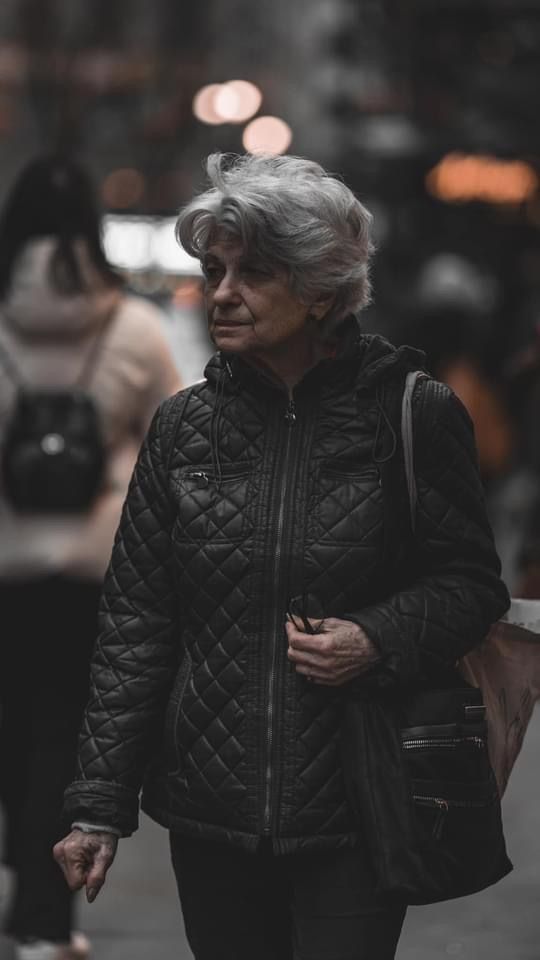 Person wearing a black quilted jacket walking on a dark city street.
