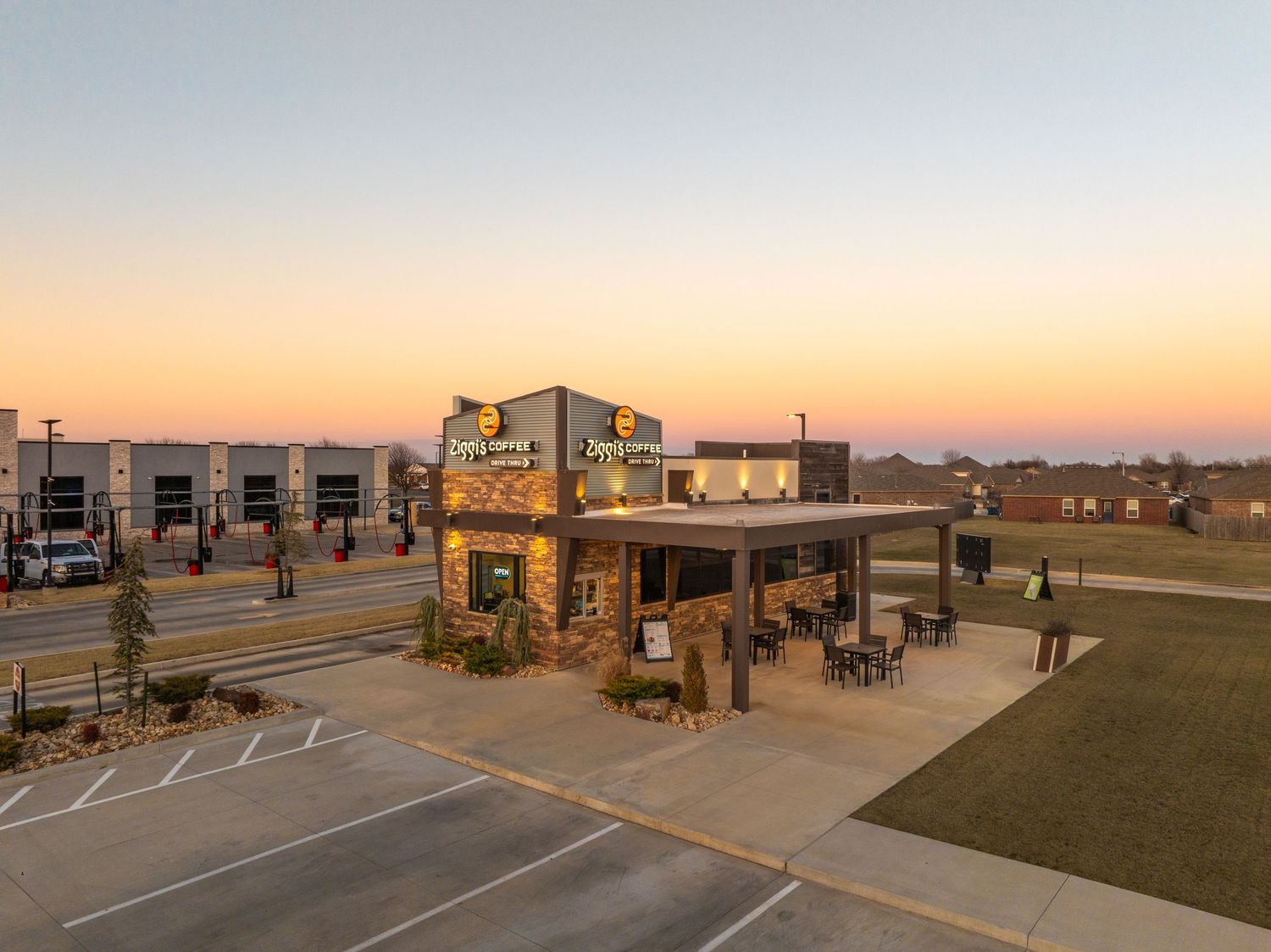 Aerial view of commercial property with parking lot and outdoor seating at dusk.