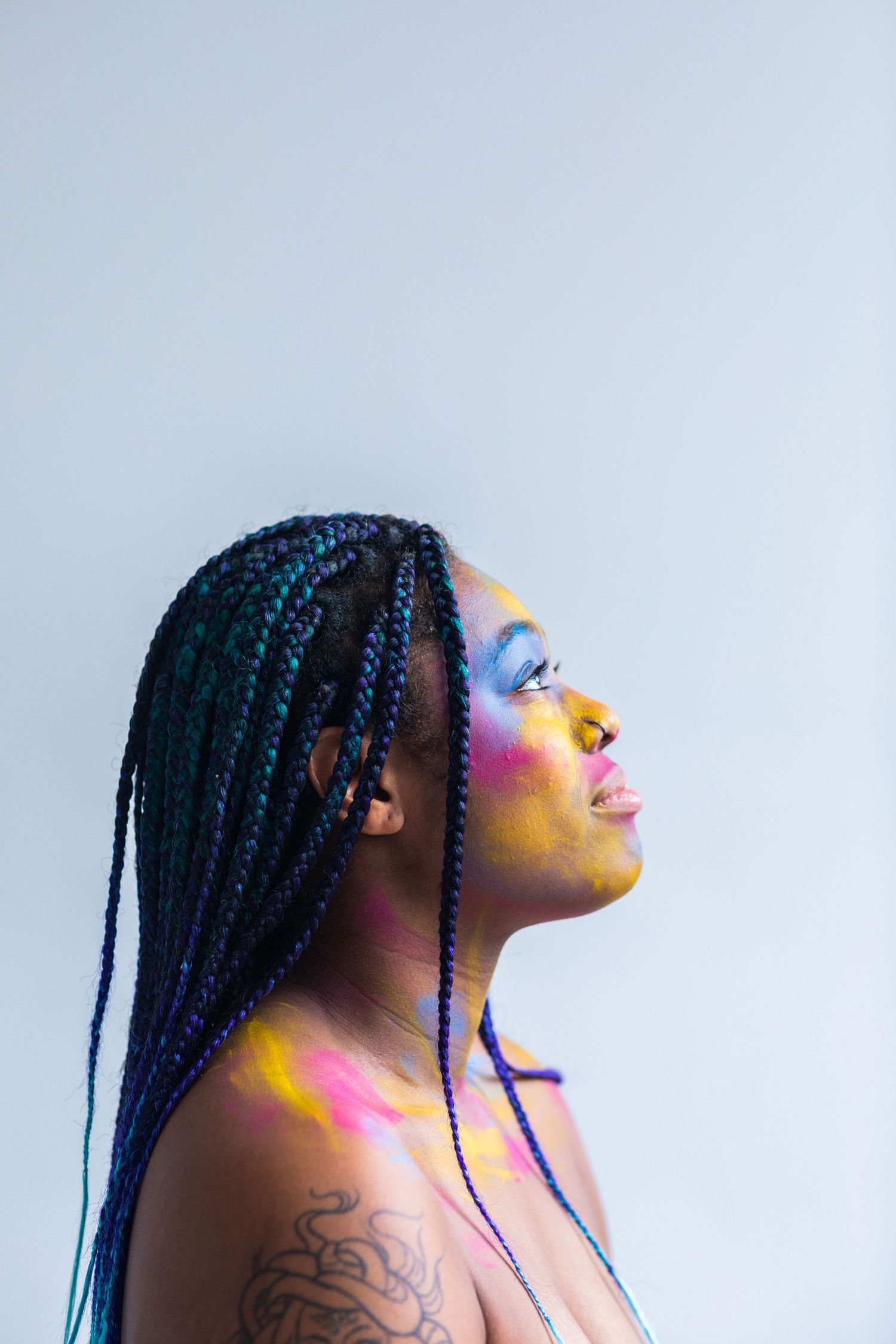 Young black woman looks towards the light as she is painted yellow, blue and pink .