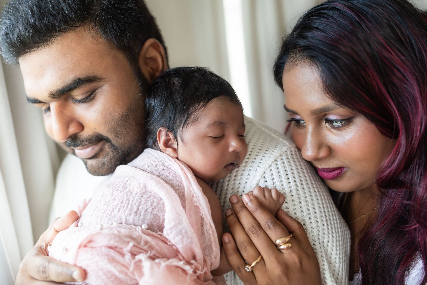 Baby rests on her father's shoulder while her mother looks at her lovingly.