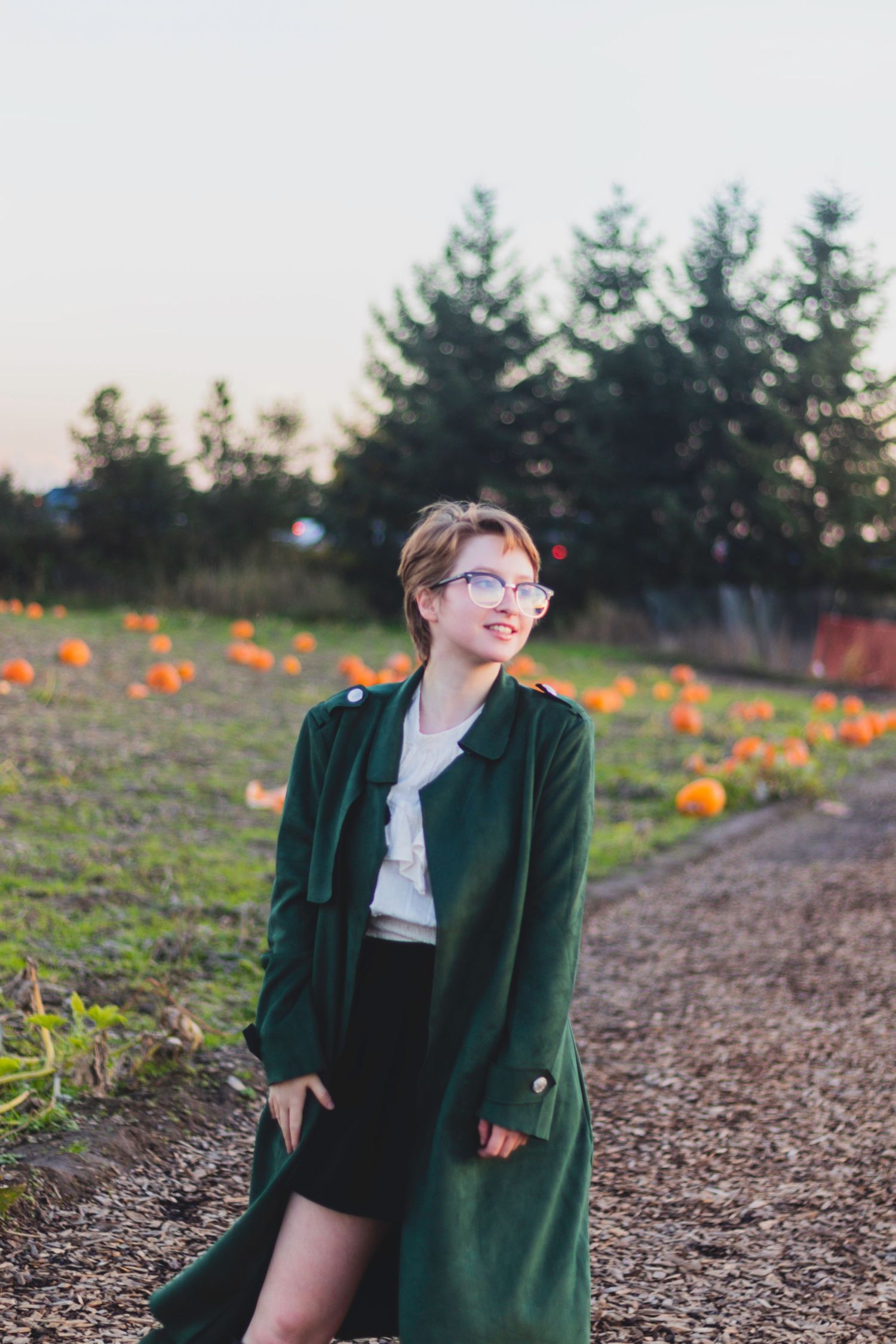 A high school senior uses her long green jacket to pose in a pumpkin patch.