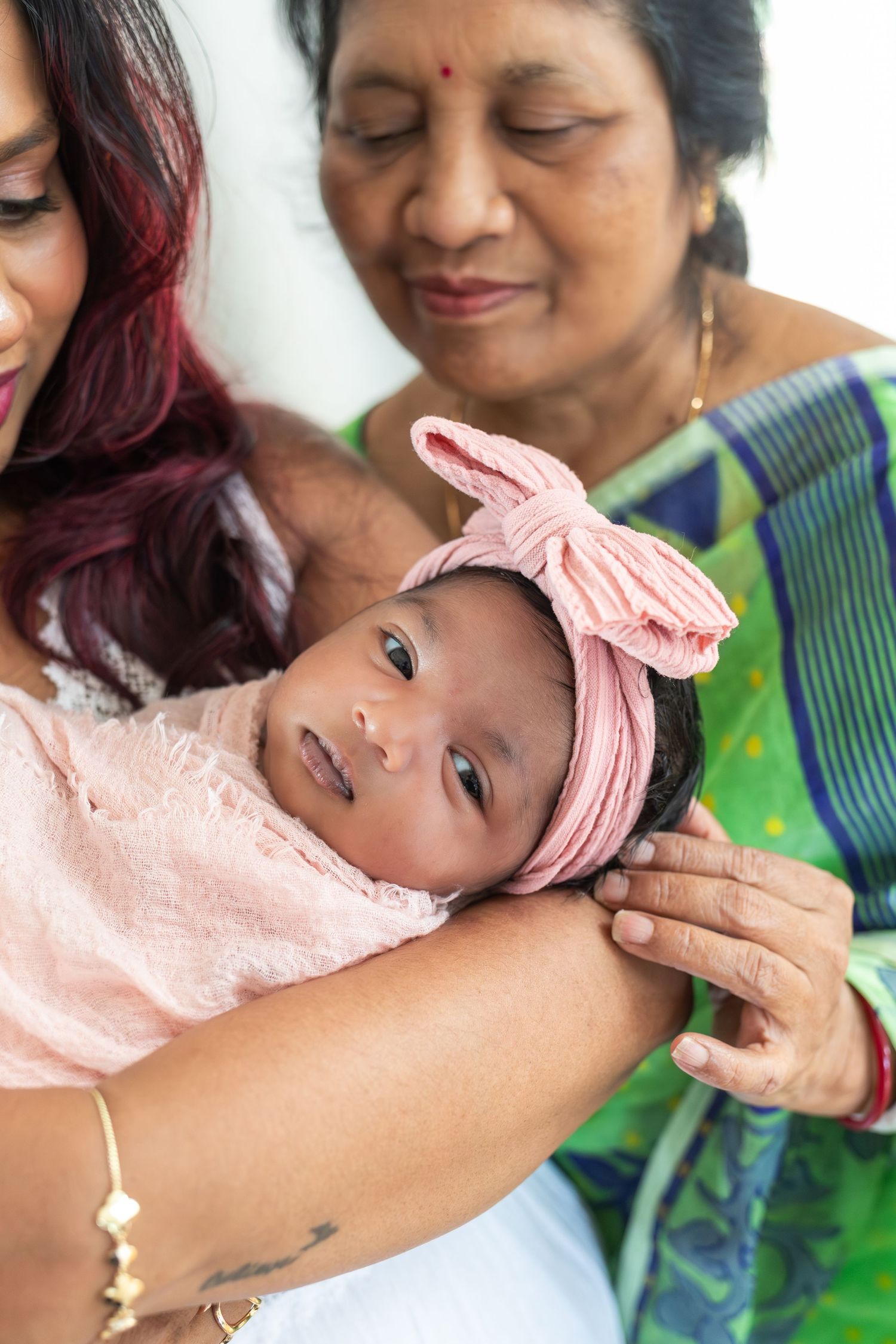 3-week old baby snuggled in her mother's arms as her grandmother looks lovingly down.
