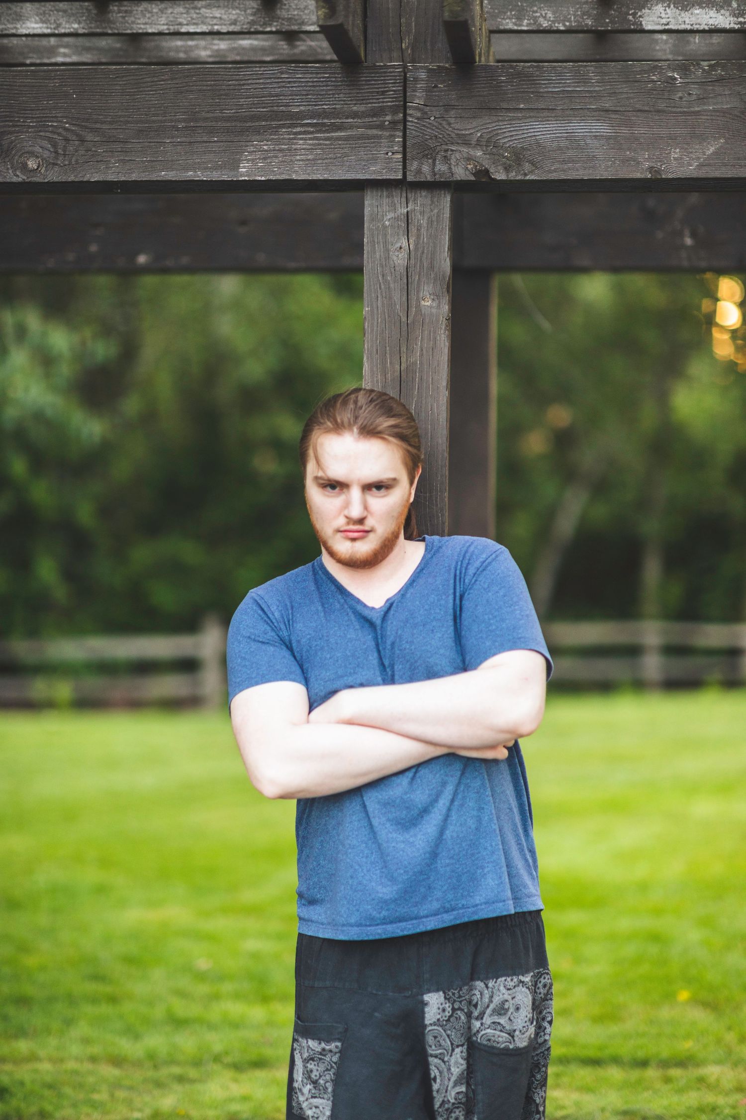 Young man wearing a blue shirt stands and smiles in front of a blurry green background.