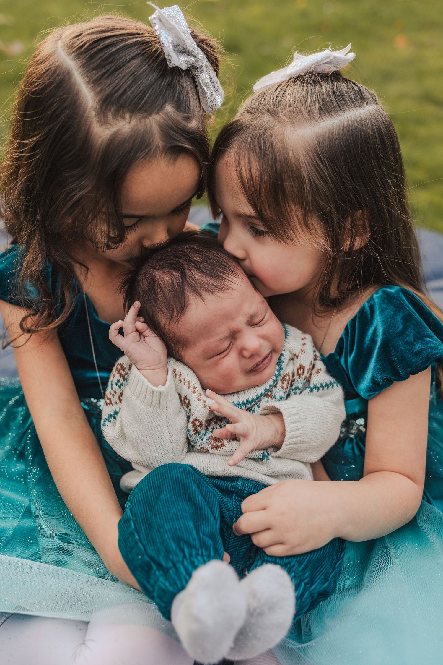 Baby boy is kissed by his big sisters.