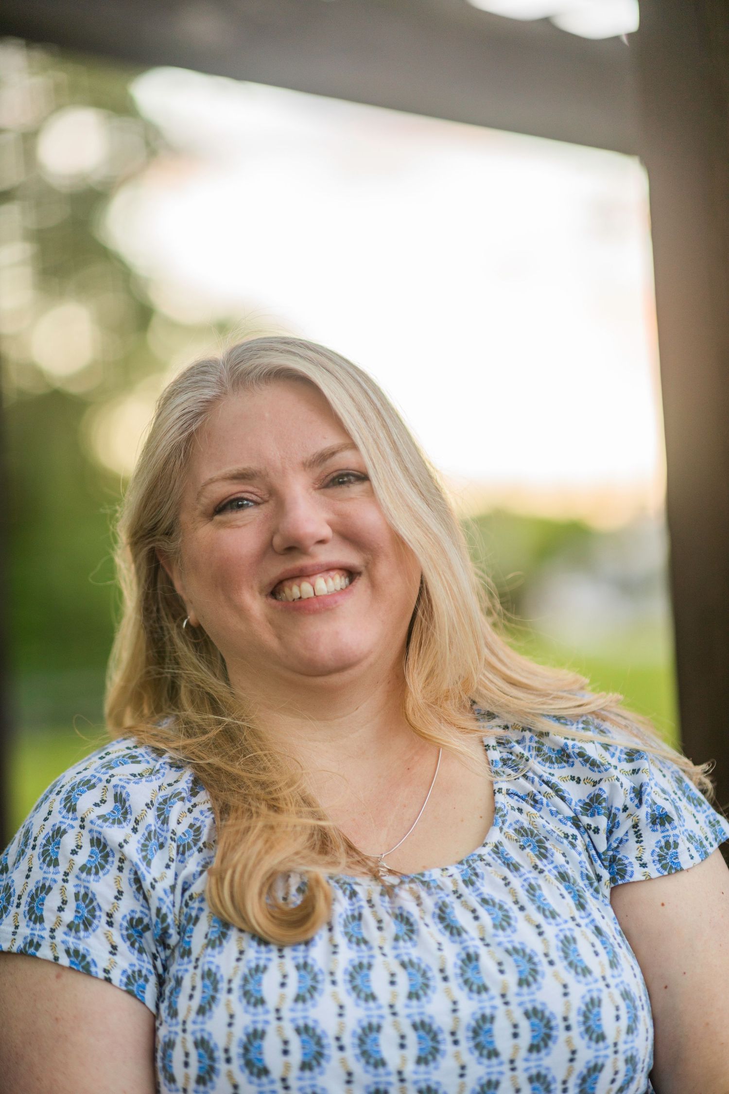 A mother smiles for the camera, wearing a blue patterned shirt.