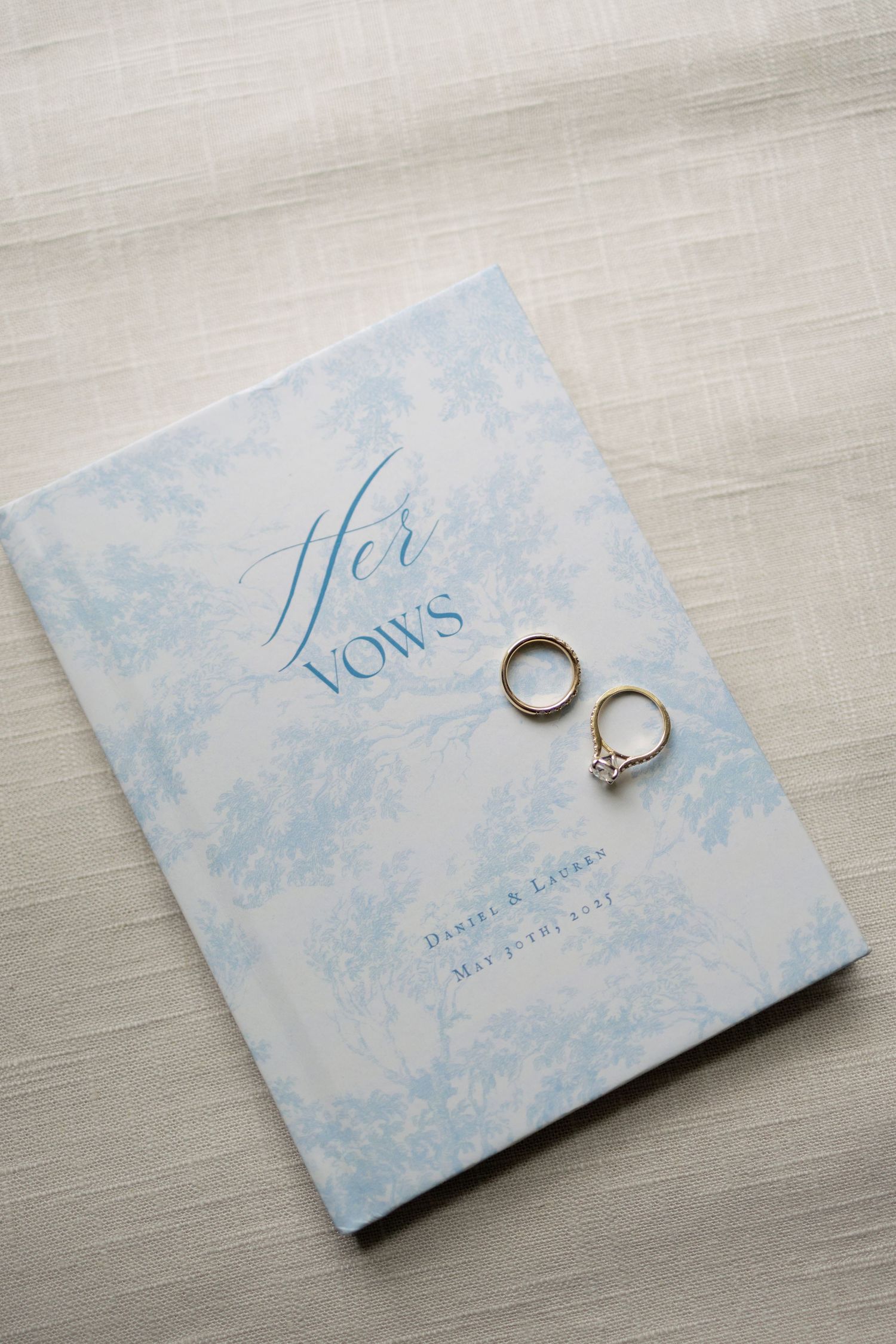 Wedding rings displayed on a pale blue and white vow book with delicate floral patterns.