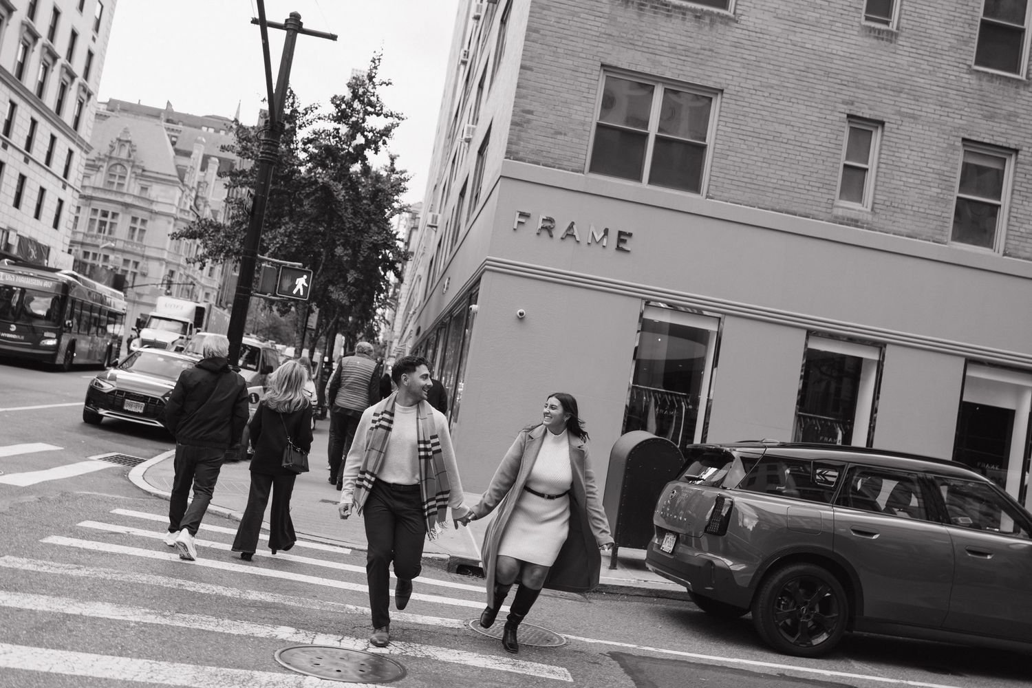 Urban street scene with pedestrians walking past storefronts in black and white.