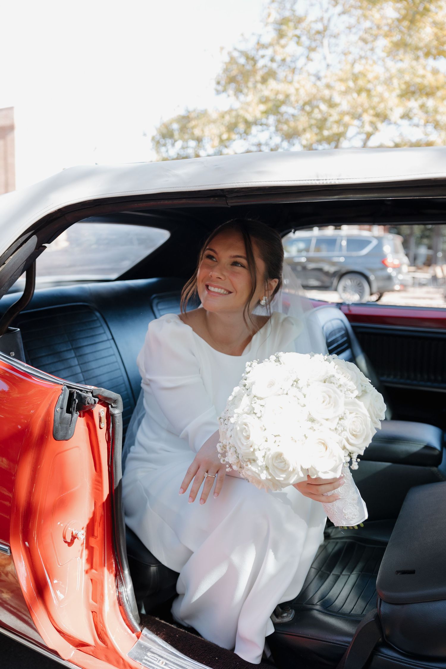 White wedding dress flowing elegantly inside a classic car with red interior.