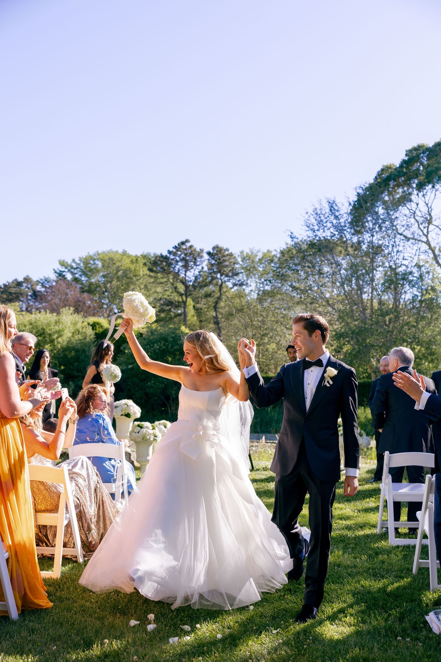 Wedding celebration with guests dancing and celebrating outdoors under blue skies.